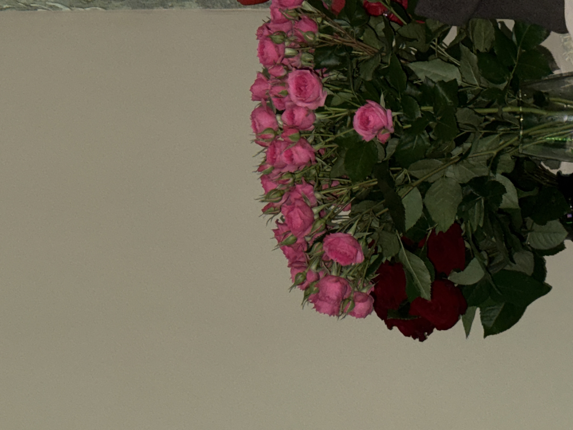 The image shows a bouquet of pink and red roses. The bouquet is positioned on the right side of the frame, against a plain, light brown background.