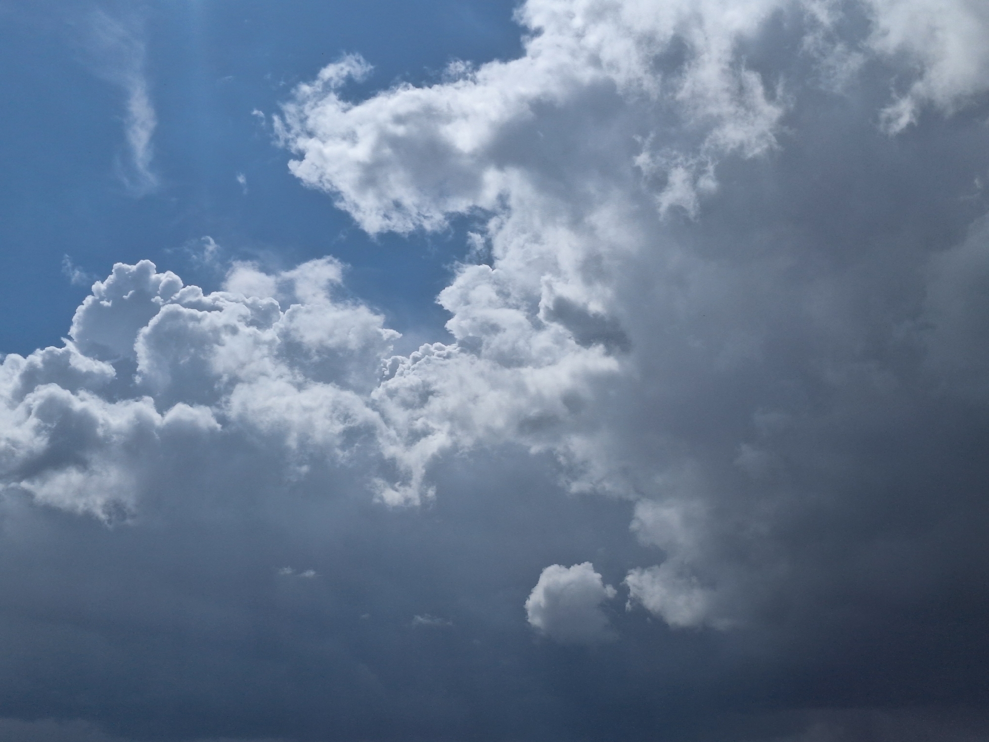 The image depicts a cloudy sky. The left side of the image contains puffy, white clouds against a patch of blue sky. The right side features large, dark, looming cumulonimbus clouds. The lighting suggests an impending storm. There are no people or objects visible, and the location cannot be verified as Tlik, Armenia, based solely on the image.
