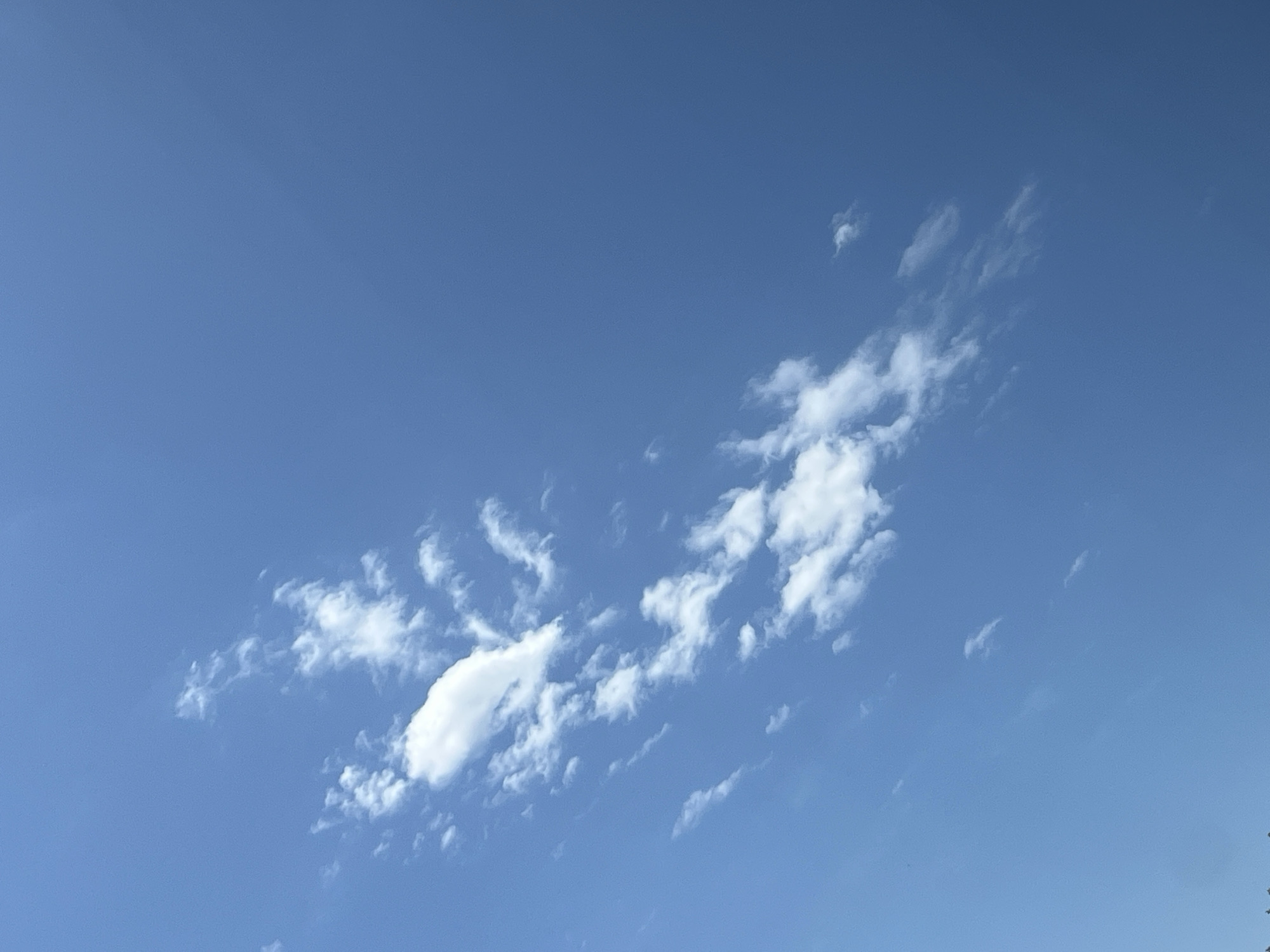The image displays a clear blue sky with scattered white clouds. The clouds are wispy and appear to be moving across the sky, possibly in a gentle breeze. There are no identifiable landmarks or structures visible, making it impossible to determine the location within Warsaw, Poland. The scene is peaceful and serene, suggesting a pleasant day. The overall impression is one of vastness and openness, typical of a clear sky on a bright day.