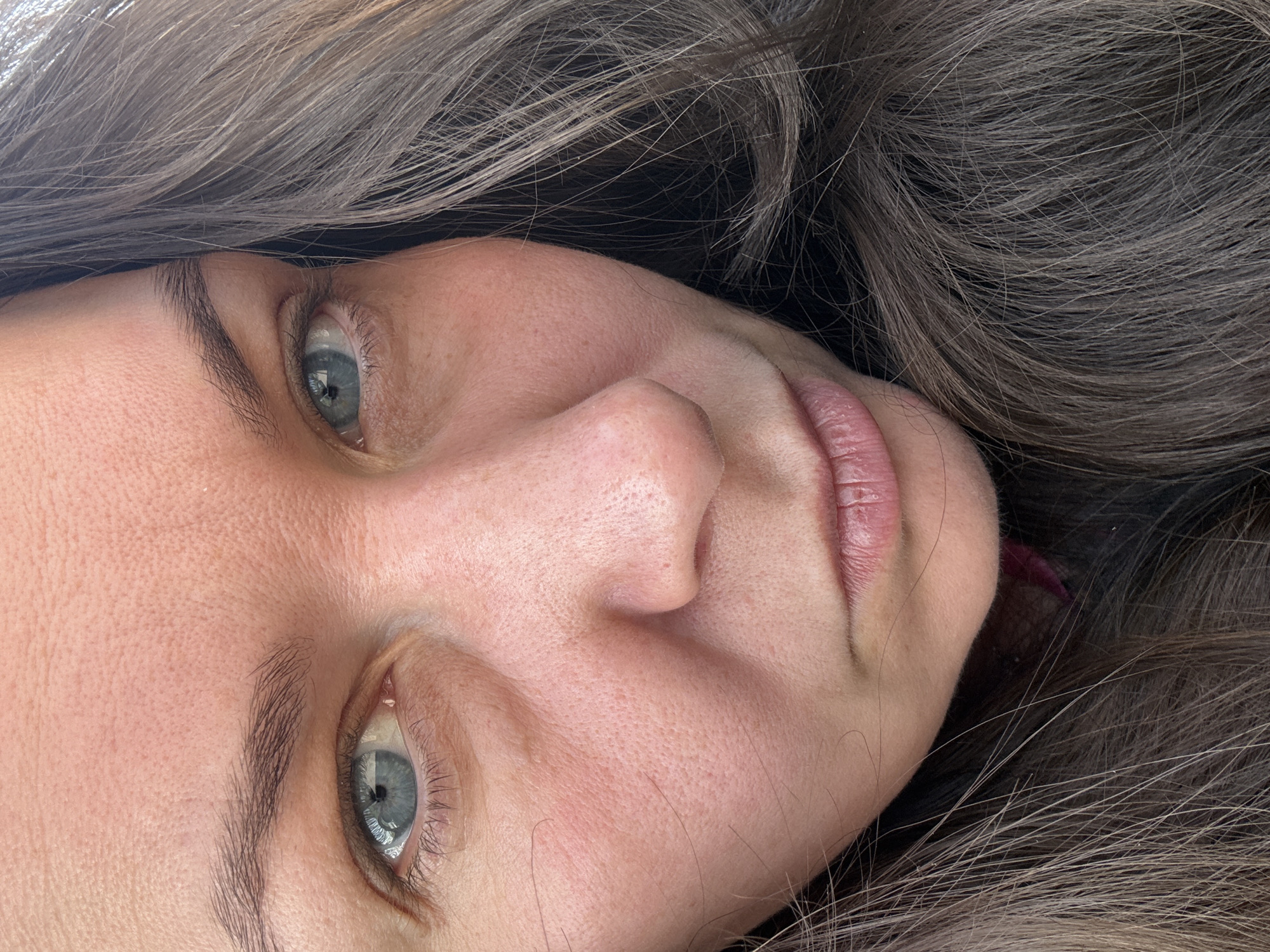 A close-up shot depicts a woman's face surrounded by dark brown or greyish-brown hair. The woman has light blue eyes and fair skin. Her lips are pink and slightly parted. No identifying details suggest a specific location in Фоки, Russia. The focus is solely on the subject's face.