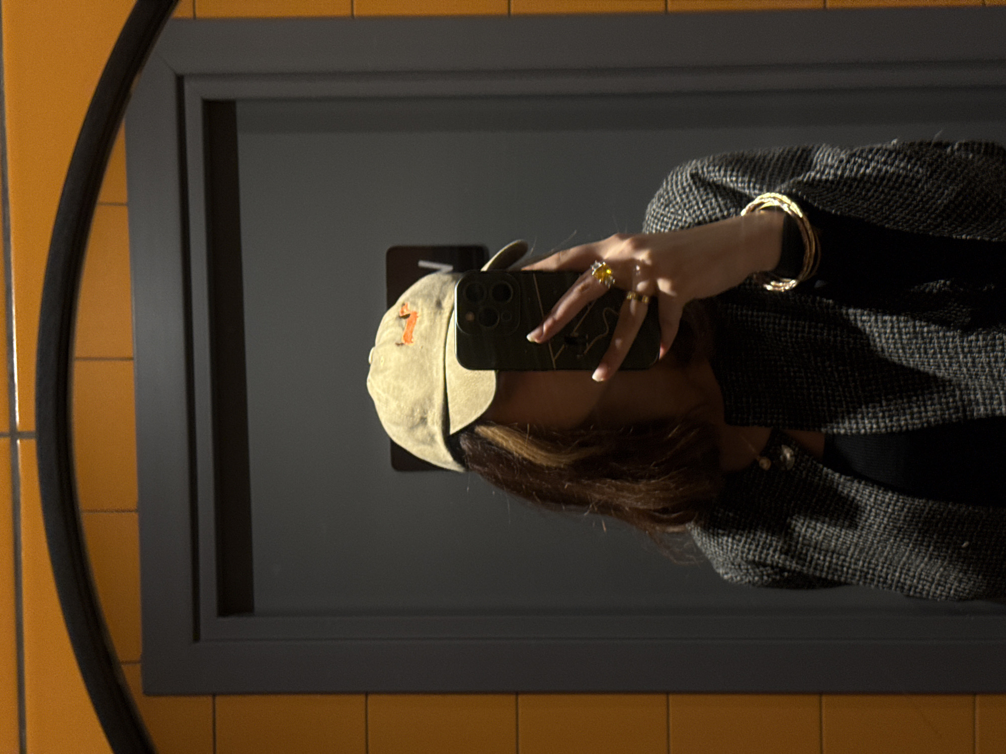 A person is taking a selfie in a mirror. The person is wearing a hat, rings, and bracelets. The background appears to be a tiled wall with a mirror. The location is unknown, and there is no information to suggest the location is in Yerevan, Armenia.