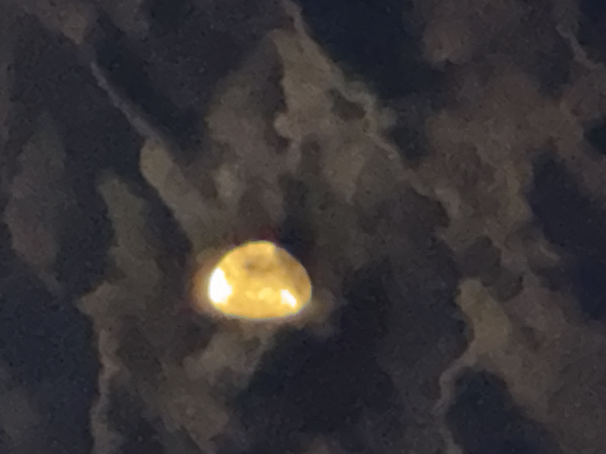 The image shows a partial view of the moon partially obscured by clouds. The moon is illuminated from the left, with a bright crescent shape visible. The clouds are dark and wispy, creating a textured background. The overall impression is of a night sky. There is no discernible location in the city of Ialoveni, Moldova. The image is too abstract to provide forensic details about people, subjects, objects, or actions.