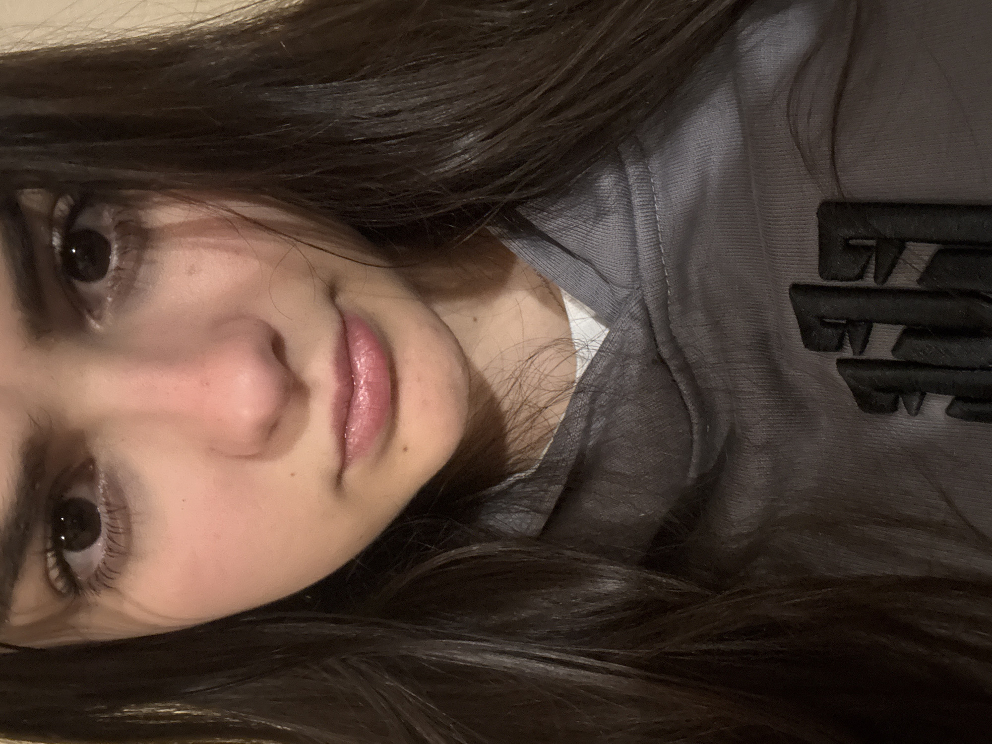 A young woman with long, dark hair is lying down, wearing a gray hoodie. The background is indistinct. There's no information to suggest this photo was taken in Blagoevgrad, Bulgaria.