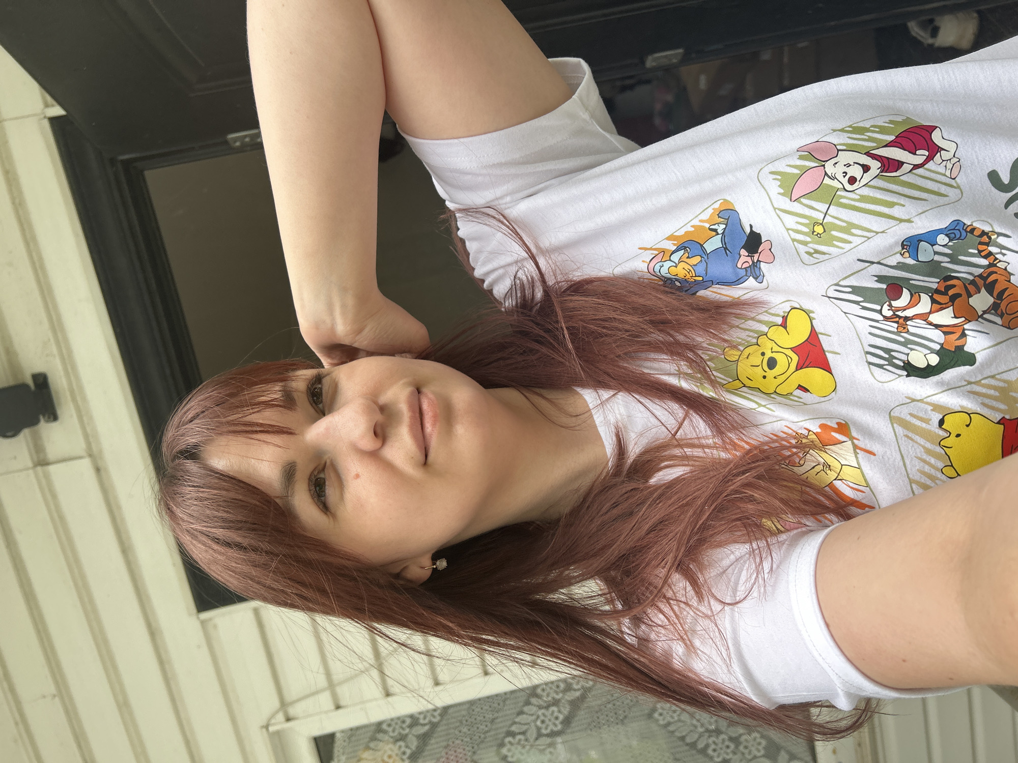 A woman with reddish-brown hair is positioned in front of a doorway, wearing a white t-shirt featuring Winnie the Pooh characters. The doorway leads to what appears to be the exterior of a building with white siding. The image does not contain enough information to determine the location of Фоки, Russia.