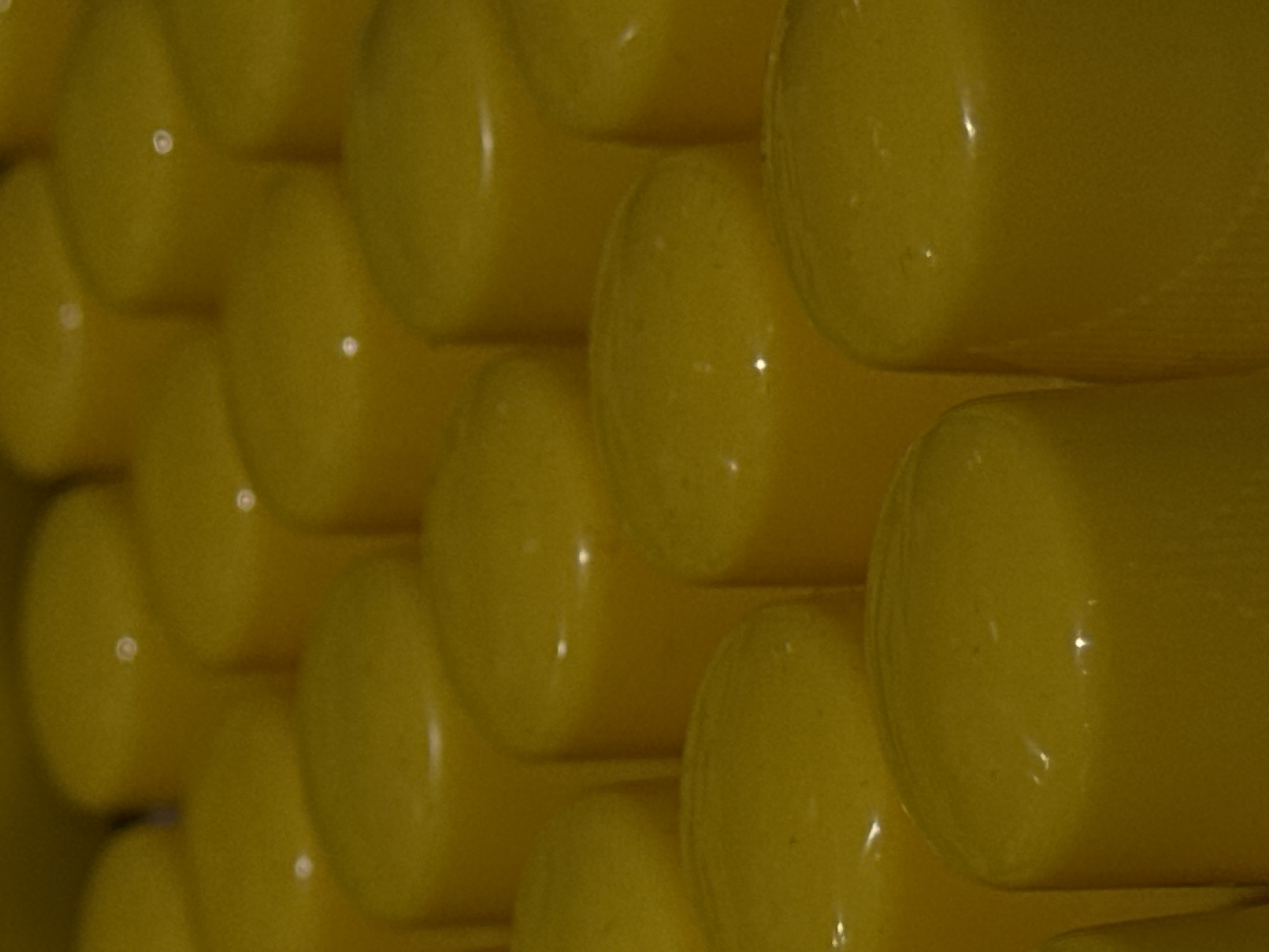 The image shows a close-up view of numerous yellow, cylindrical objects, possibly candies or small food items, arranged in rows. The lighting creates reflections on the smooth surfaces of the objects, giving them a glossy appearance. The background is out of focus, emphasizing the texture and color of the items in the foreground. There is no discernible urban environment or identifiable Moscow landmarks.