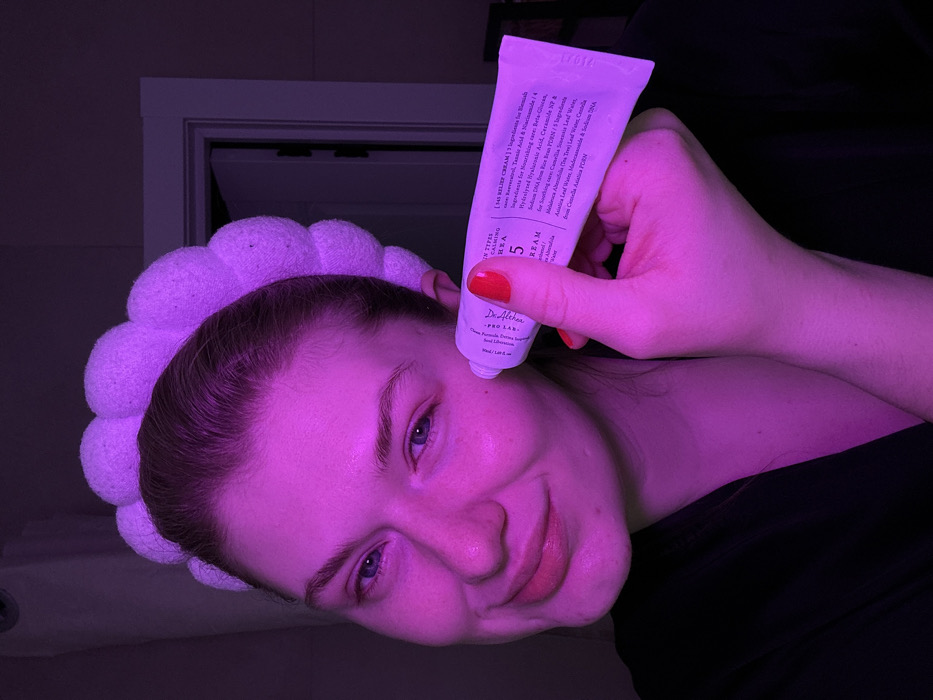 A woman with a plush headband applies Dr. Althea Pro Lab 5 cream. The product is identified as "[143 RELIEF CREAM]," emphasizing ingredients for calming, nourishing, and soothing care, including niacinamide, hyaluronic acid, ceramide, rice bran, camellia sinensis leaf water, and centella asiatica. The overall image has a strong purple hue.