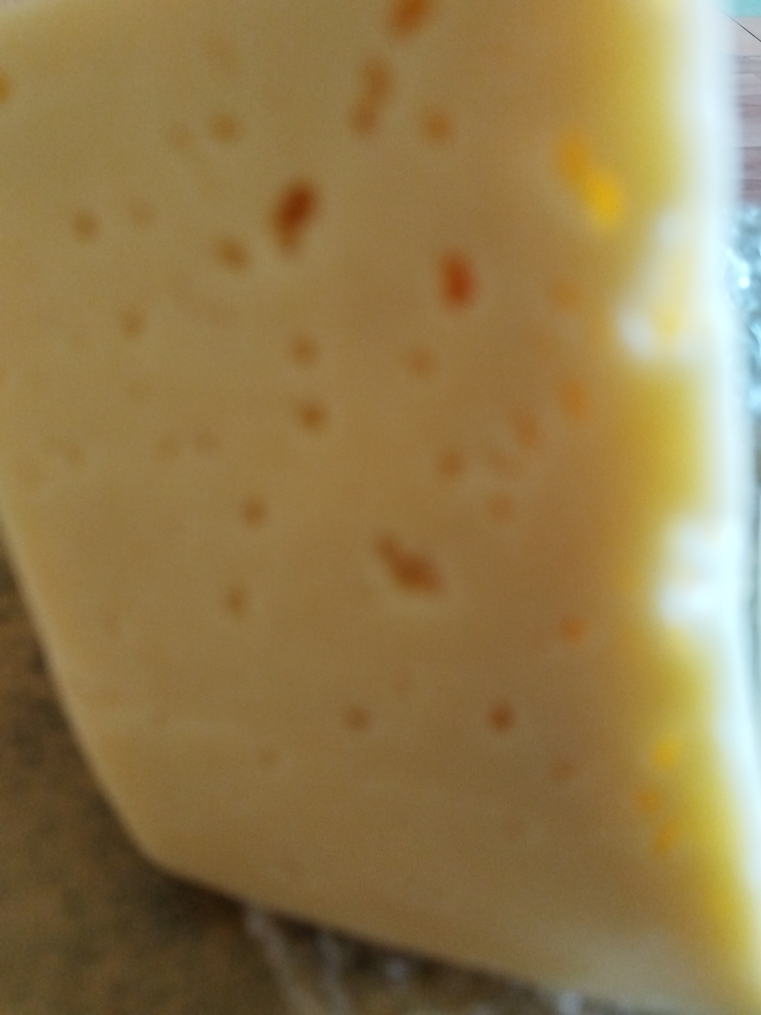 A blurry, close-up photograph shows a wedge of light-colored cheese with small holes or spots. The cheese appears to be wrapped in clear plastic. The exact type of cheese cannot be determined due to the image's poor resolution.
There's no evidence indicating the photo was taken in Chaikovsky, Russia.