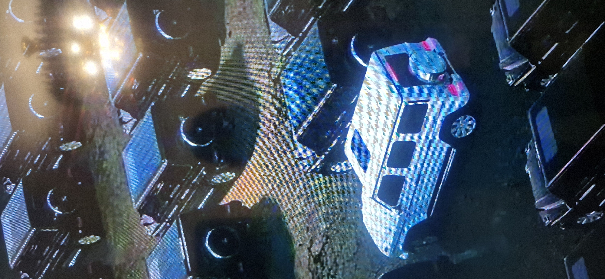 The image depicts an aerial view of a car parking lot, likely located in an urban area of Unknown, Unknown. Several vehicles, primarily black SUVs, are parked in an organized manner. A white van is also visible, parked alongside the other vehicles. The scene appears to be set at night, with artificial lighting illuminating the parking lot. The environment is urban, suggesting a developed area within the city. There is no indication of any individuals, actions, or specific interactions in the image.