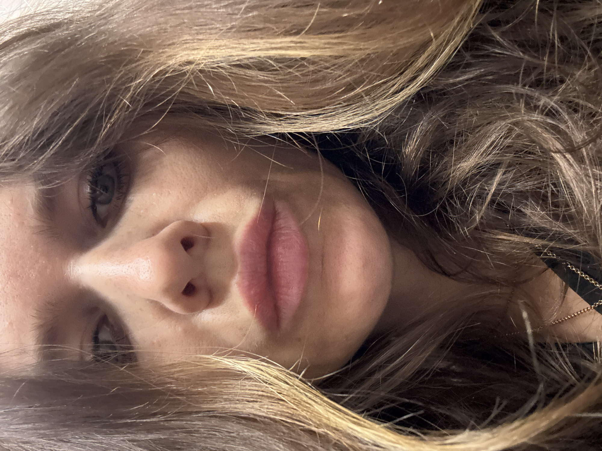 The image shows a close-up view of a woman's face, tilted to the side, with her hair surrounding her face. The hair is light brown with blonde highlights. Her eye is visible, appearing light-colored. Her lips are full and pink. The background is dark and out of focus. The presence or absence of a Moscow, Russia, location cannot be determined from the visual information.