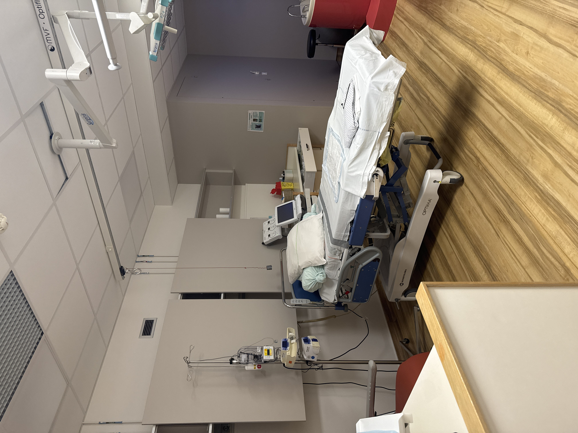 The image depicts a medical examination or treatment room, likely in a hospital or clinic, in Tourcoing, France. The room is equipped with a hospital bed, a medical cart with various devices, and overhead surgical lights. The overall impression is one of a sterile and functional environment.