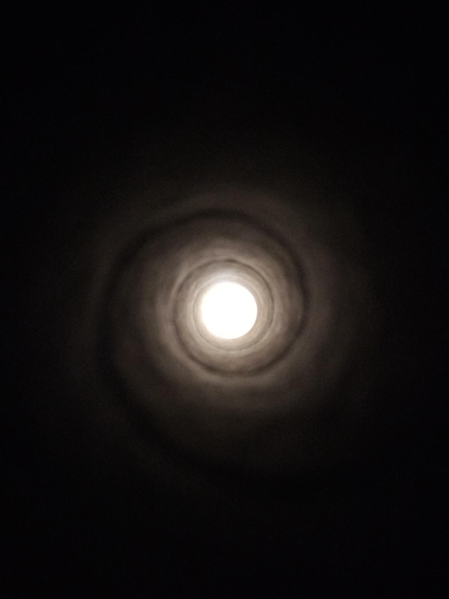 The image is a low-angle shot looking up into a dark, cylindrical shaft or tunnel. A bright light source is visible at the far end, creating a luminous circle. The walls of the shaft appear to be textured and are illuminated by the light, showing a swirling pattern that fades into darkness. The overall impression is of looking into an abyss or a void with a distant light. The location in Kremenchuk, Ukraine cannot be determined from the visual information provided.