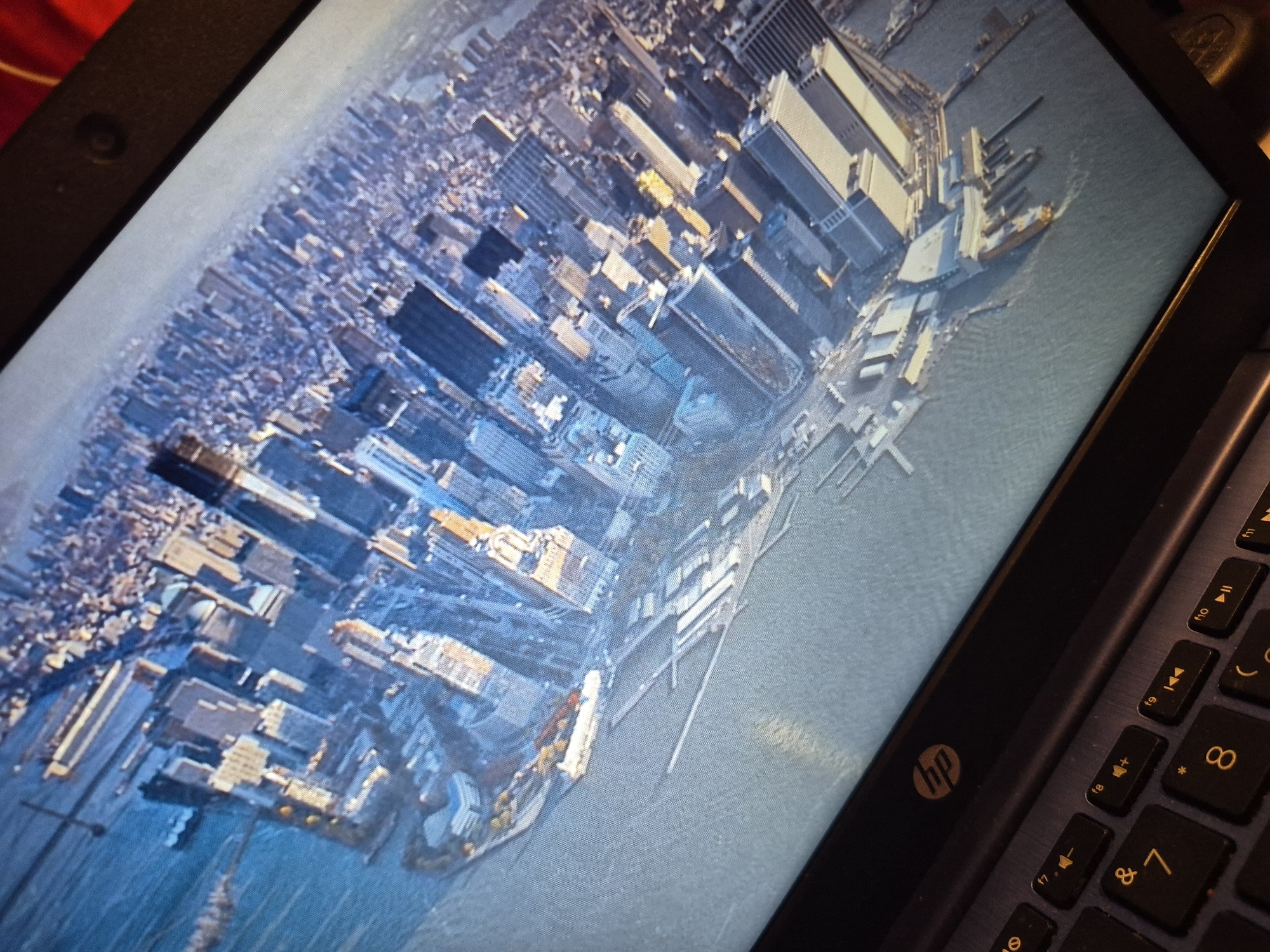 The image shows a close-up view of a laptop screen displaying an aerial photograph of a dense urban landscape, likely a city skyline, with a body of water in the foreground. The buildings are tall and tightly packed, suggesting a major metropolitan area. The angle of the photograph is from above, looking down and slightly to the side. The laptop itself is visible at the bottom of the image, with its keyboard and the HP logo clearly discernible. The screen is bright and displays the city scene with sharp detail. The context of Sandwell, United Kingdom, is not supported by any visual evidence in the image.