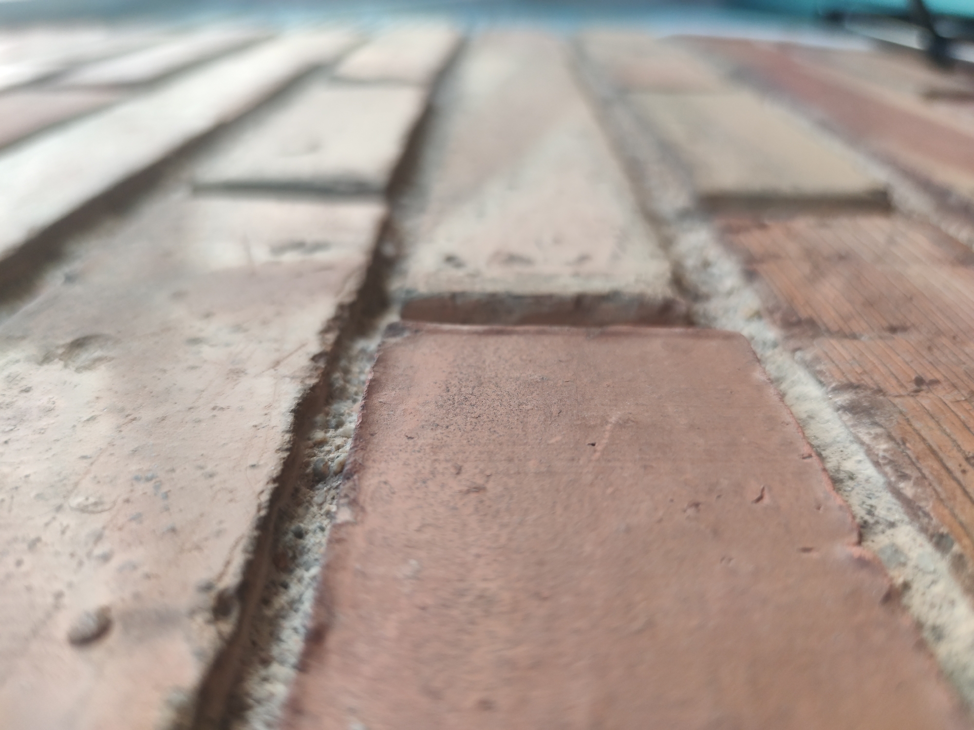 The image shows a close-up view of a brick surface with mortar joints. The bricks are reddish-brown in color and have a slightly textured surface. The mortar joints are gray and appear to be slightly recessed. The image is taken at a low angle, giving the surface a sense of depth and perspective. The location is unknown.