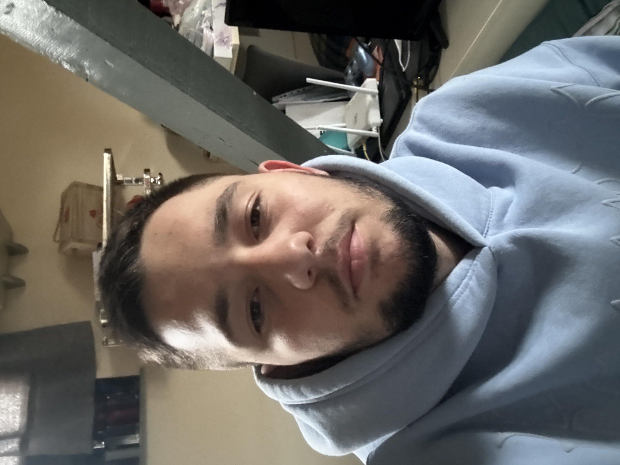 A person is wearing a light blue hoodie. The background includes a beam or edge of a wall, possibly a ceiling or a loft-style space. In the background, there is also some equipment like a router. The location in Sofia, Bulgaria, cannot be determined from the image.