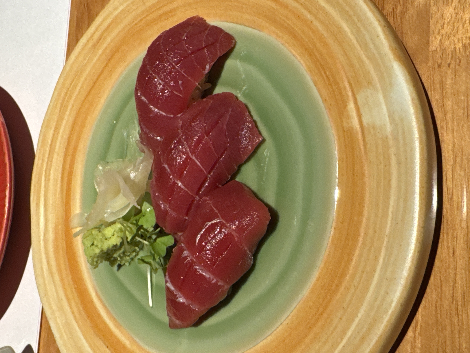 The image shows a plate of tuna sashimi, accompanied by wasabi and pickled ginger, served on a green and brown rimmed plate. The scene is likely in a restaurant or dining establishment, given the presentation of the food. The location is not discernible from the image itself, and therefore cannot be identified as Yuexiu District, China, or anywhere else specifically.