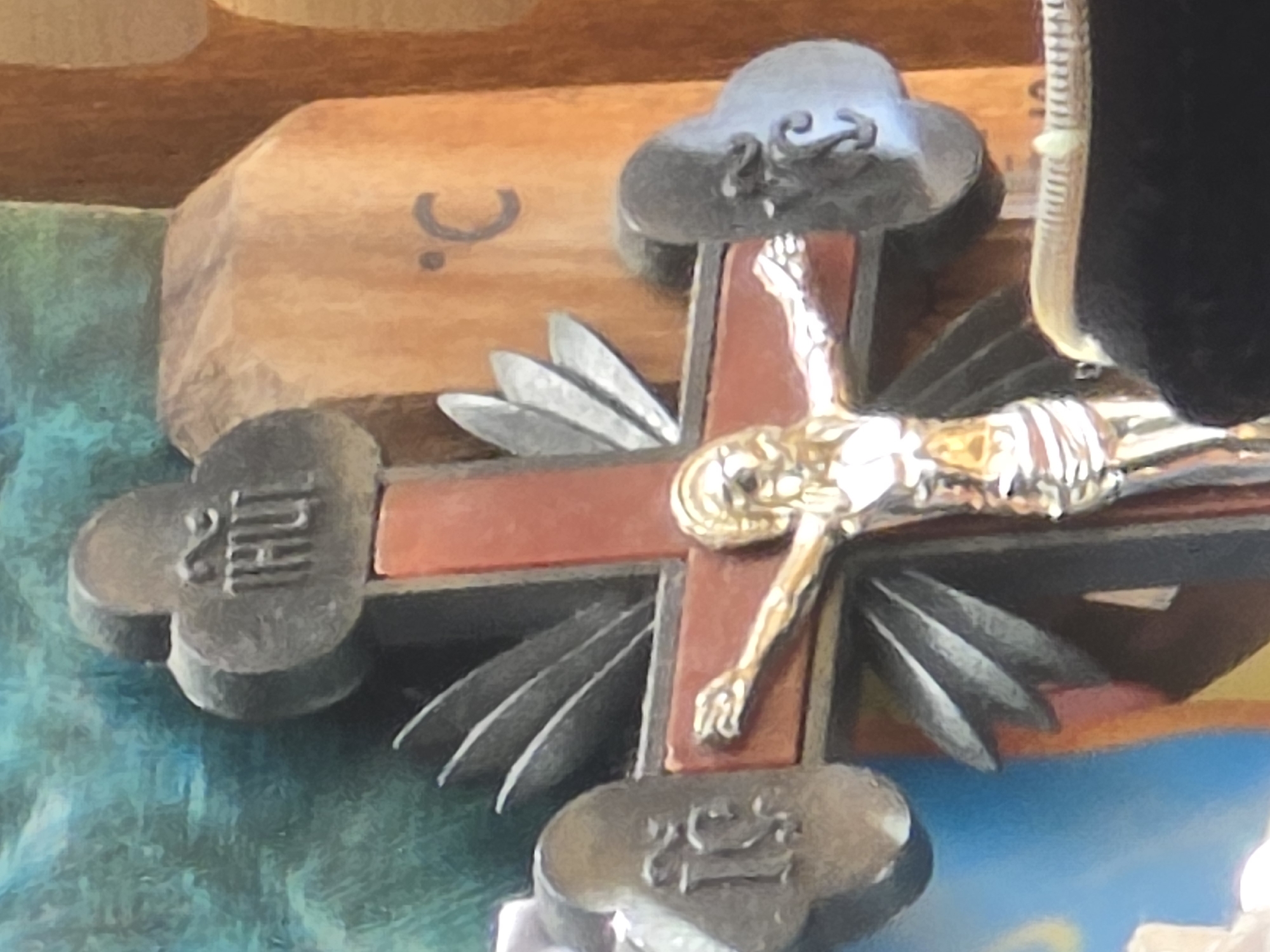 A close-up, low-angle shot depicts a crucifix with a golden figure of Jesus. The crucifix is adorned with metallic embellishments at the ends of its arms and at the top. The top embellishment has the word "THUL" inscribed on it. To the right of the crucifix, on a wooden surface, is the symbol for degrees Celsius, "°C". The background features a textured, green surface on the left and a wooden surface on the right.