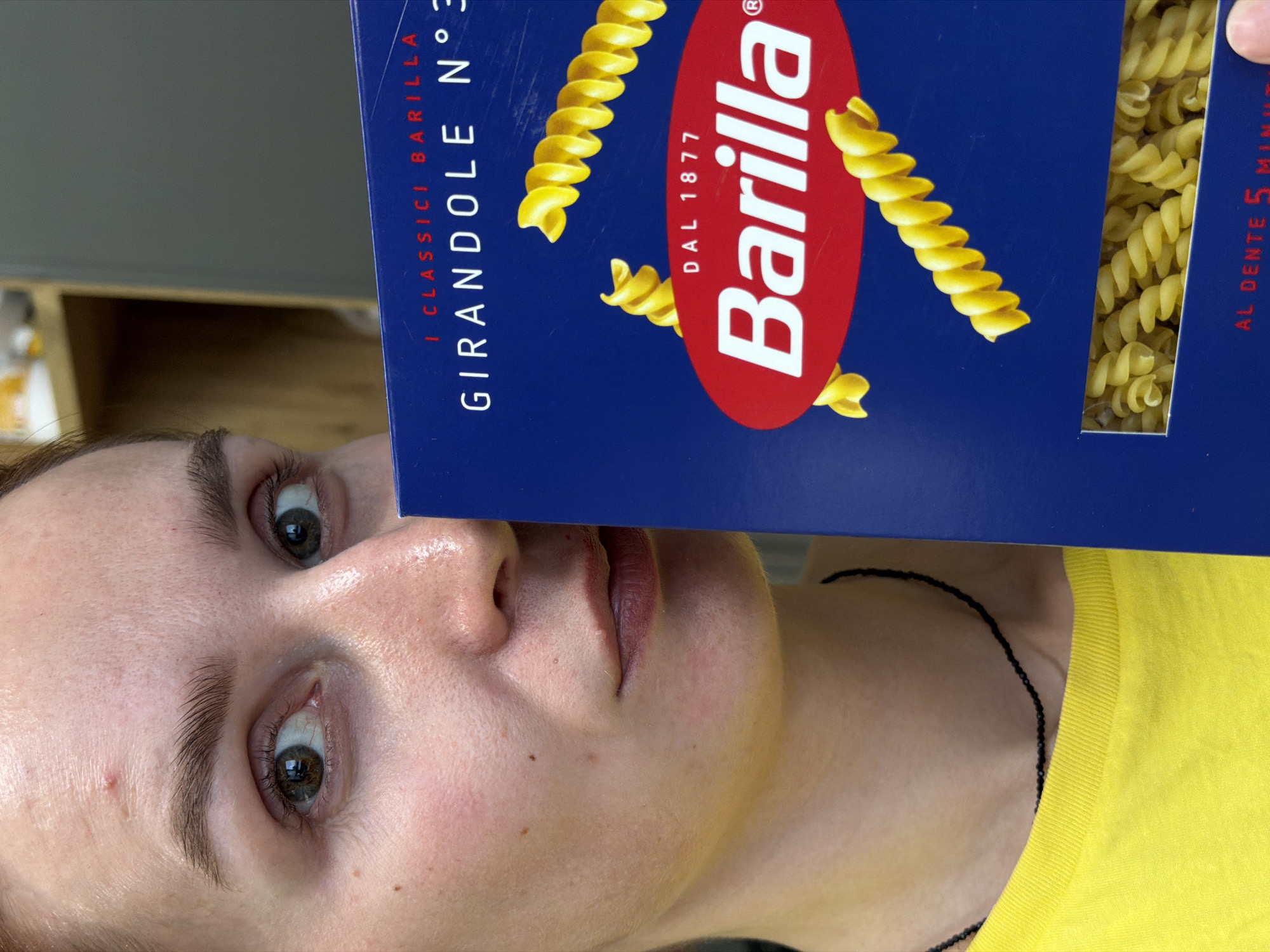 A woman is holding a box of Barilla Girandole N°3 pasta in front of her face. The pasta box is blue with a red oval containing the word "Barilla" in white letters. The city of Chaikovsky, Russia is not identifiable in this image.