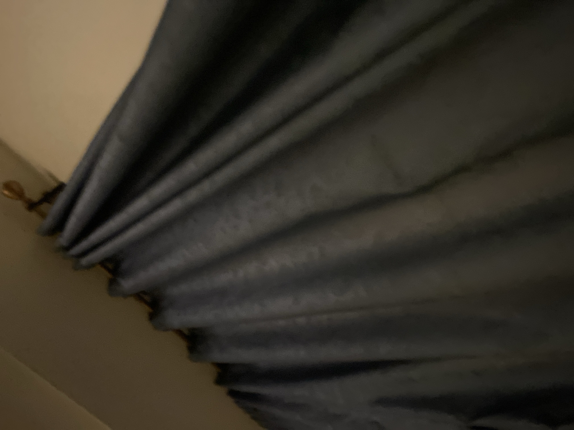 The image shows draped, grey curtains hanging from a gold-colored curtain rod. The wall behind the curtain is light tan. The location is not identifiable as being in Abuja, Nigeria, based on the visual information in the image.
