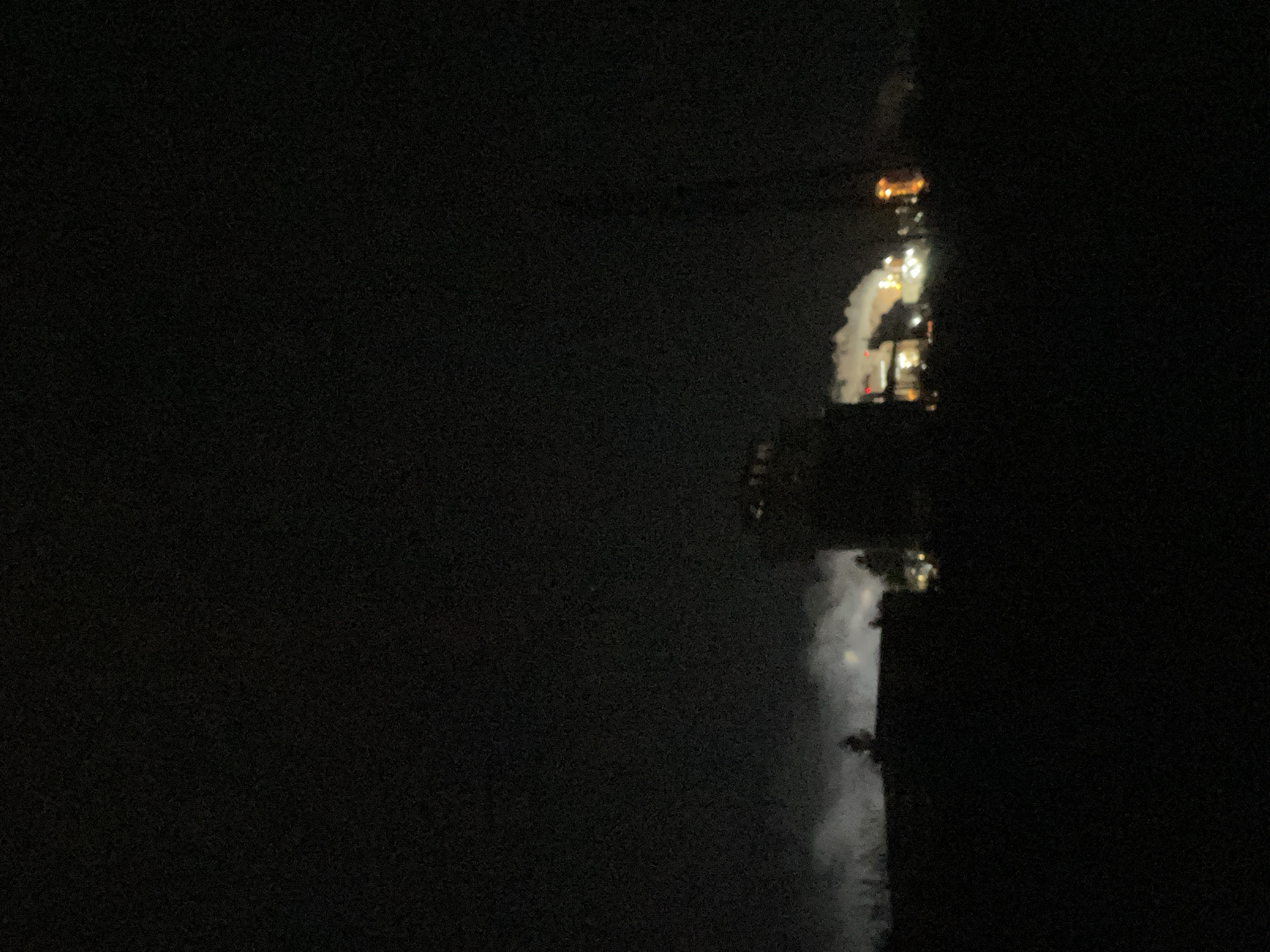 At night, lights illuminate a building and its reflection in water, likely a lake or river. The environment surrounding the location is dark and obscured. It is not possible to precisely identify the location in Razgrad, Bulgaria.