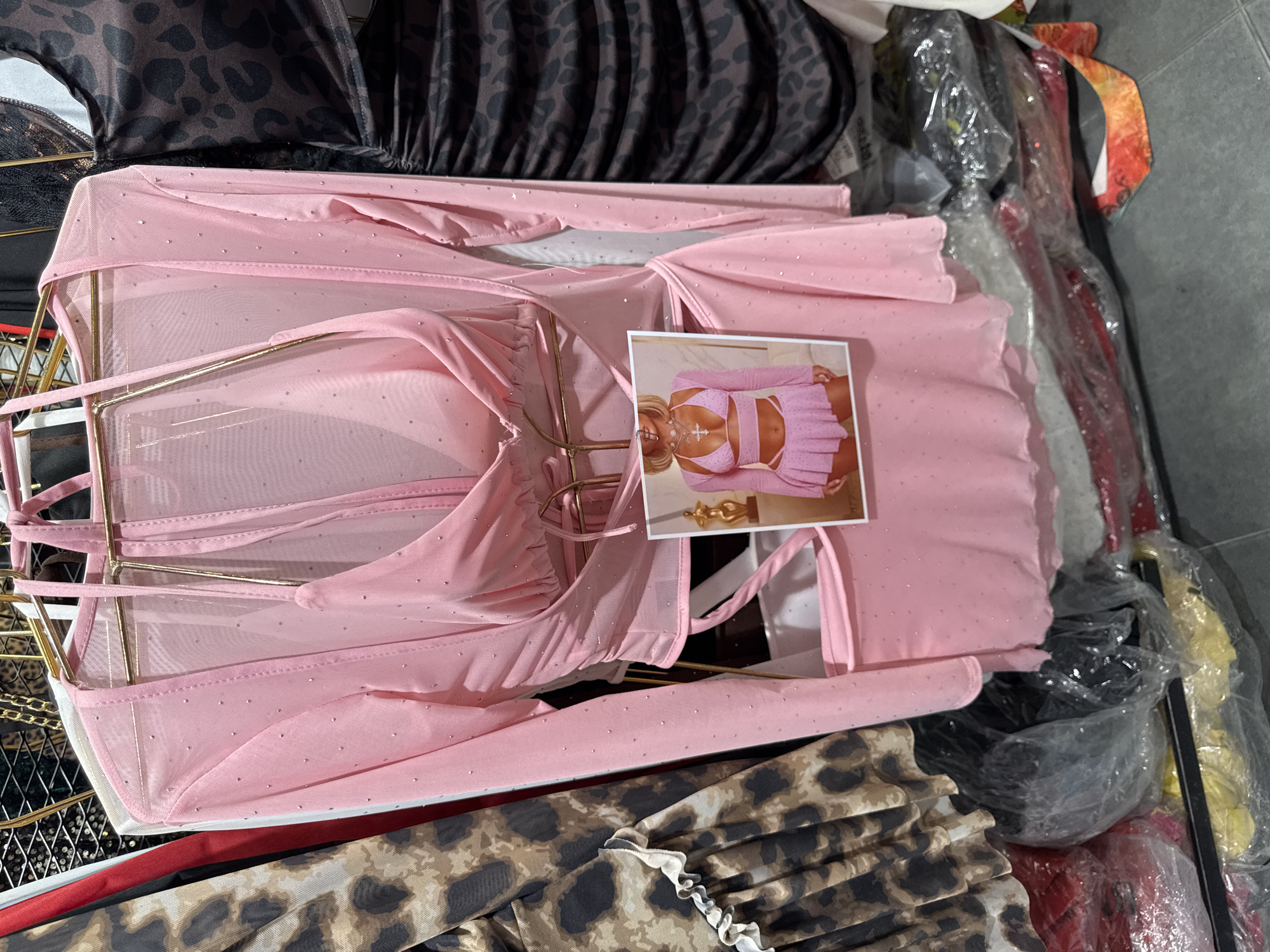The image shows a pink sparkly see-through dress on a mannequin or display in a store. The dress has a halter neck and a cutout design. A photograph of a woman wearing a similar pink outfit is attached to the front of the dress. The store appears to be in Gungoren, Turkey, with other clothing items visible in the background.