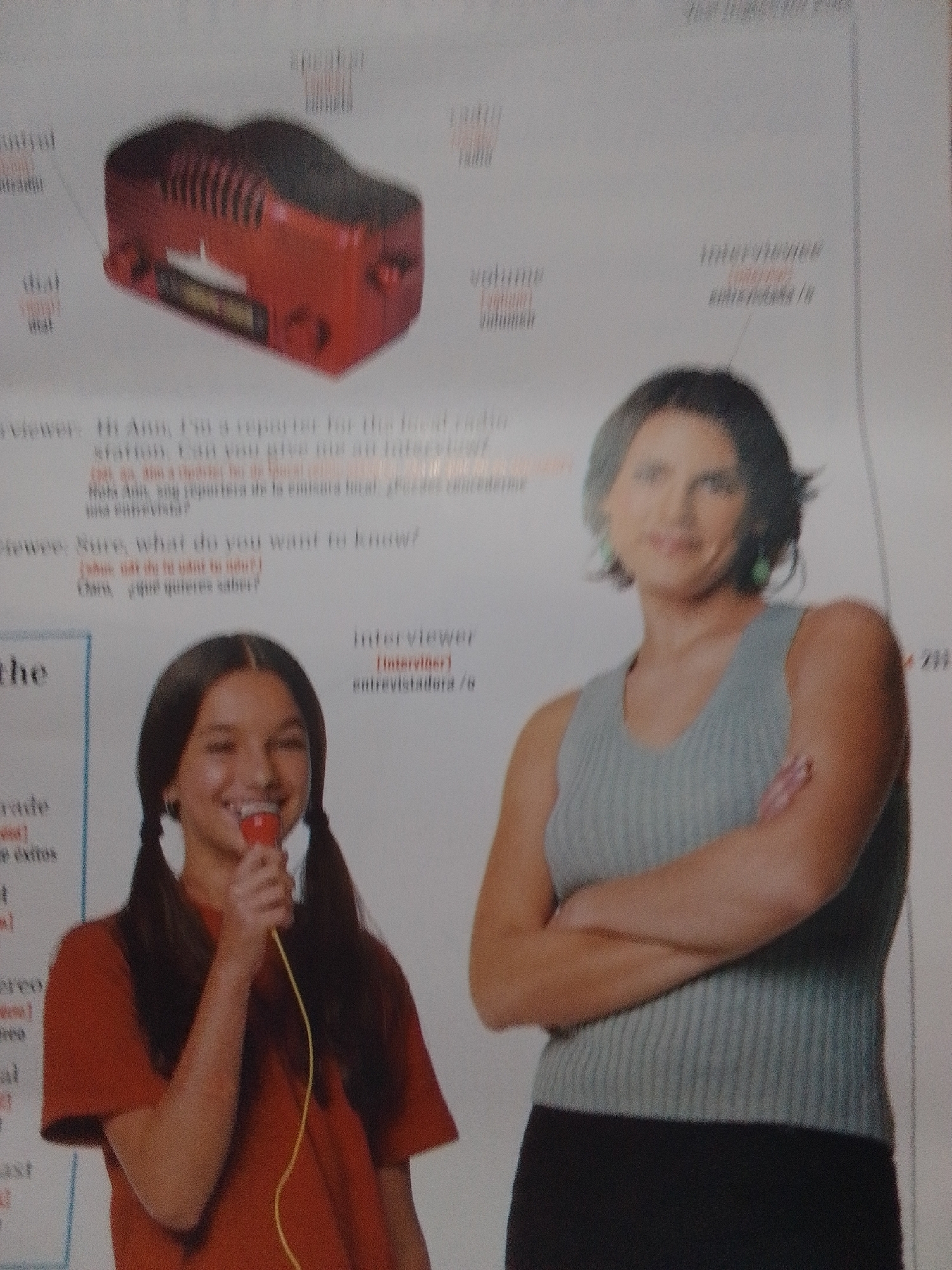 The image shows two women, one holding a microphone and the other with her arms crossed. The background features text and diagrams related to a radio and its components. The woman with the microphone is wearing a red shirt, and the other woman is wearing a grey sleeveless top and a black skirt. The scene appears to be a page from a textbook or magazine, with educational content about radio operation. There is no visible indication of the location being La Tagua, Venezuela.