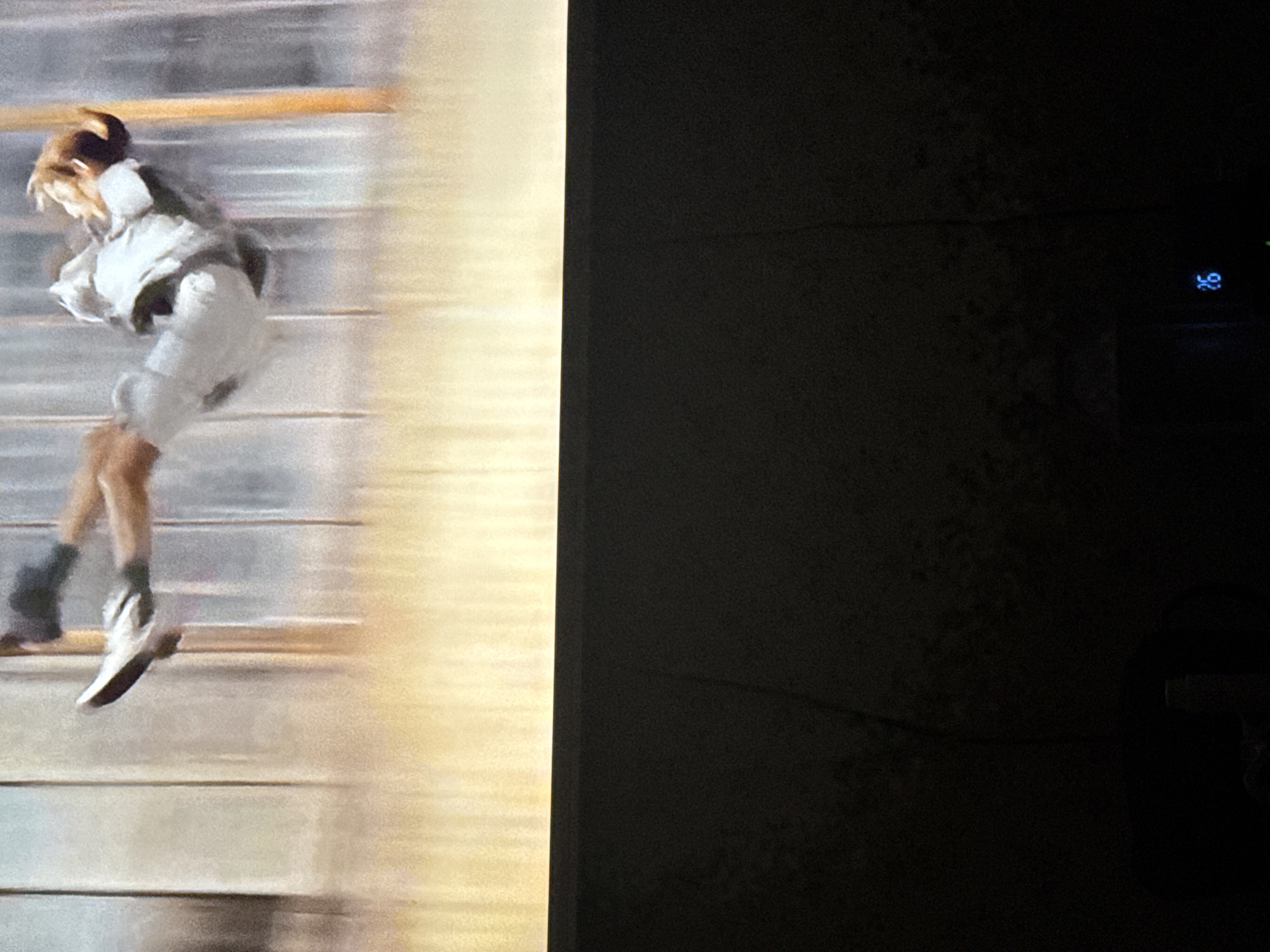 The left side of the image depicts a blurry figure, presumably a person, in motion. They are wearing light-colored clothing, including shorts and a jacket, and dark socks with white shoes. The background behind the figure appears to be a series of horizontal lines, possibly stairs or a wall with slats, suggesting movement or speed. The overall color palette is muted with beige and white tones.
The right side of the image is completely black, obscuring any details of the surrounding environment.
There is no information in the image to identify the location. Therefore, it is not possible to describe the scene in detail, including the location in the city of Mytishchi, Russia.