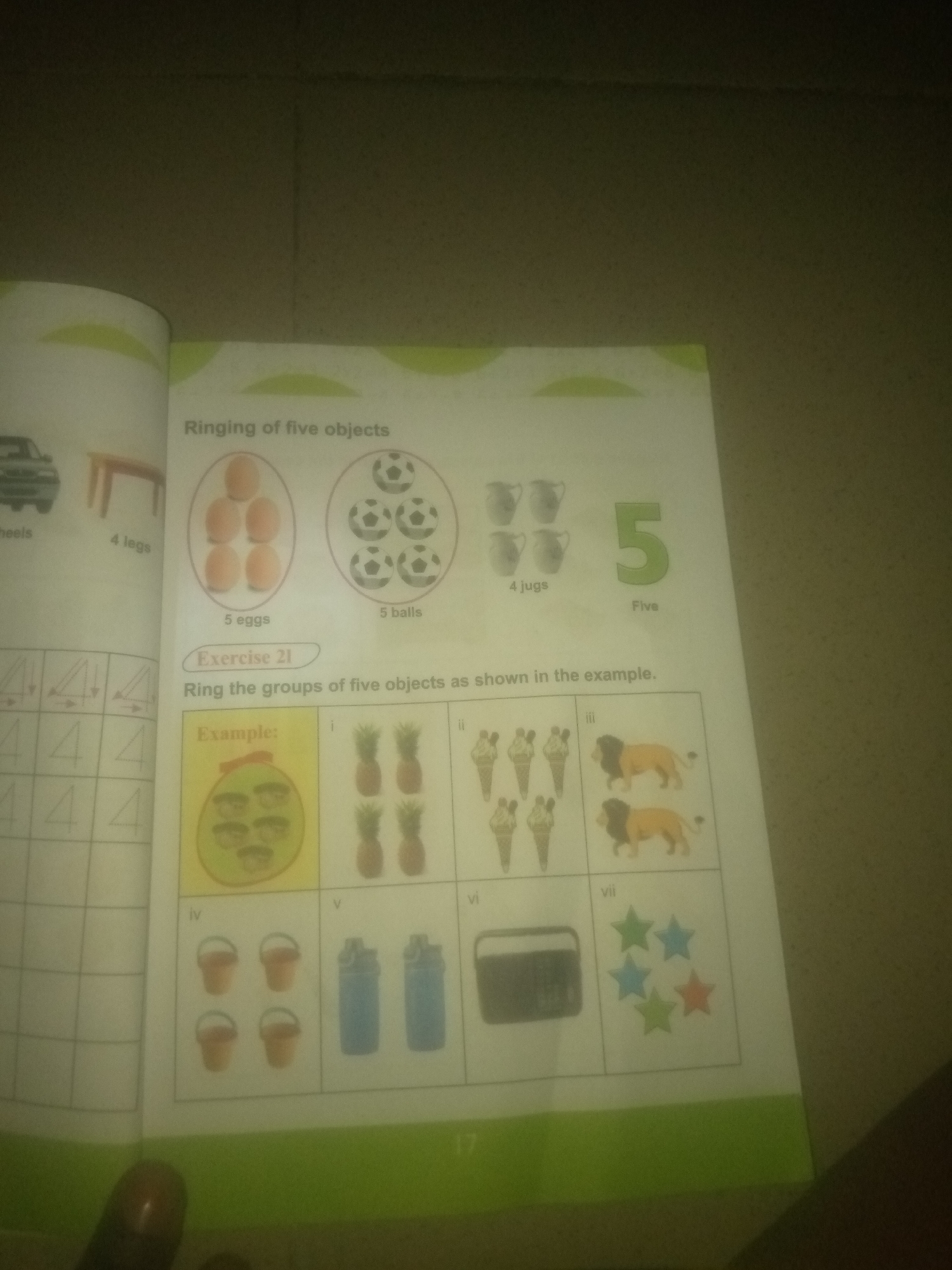 The image is of a page from a children's educational book. The page is titled "Ringing of five objects" and includes examples of groups of objects, with some circles containing five items and others containing fewer. Below this section is an exercise labeled "Exercise 21" with the instruction "Ring the groups of five objects as shown in the example." The exercise presents several boxes labeled with Roman numerals (i through vii), each containing a different collection of objects. The objects shown include pineapples, ice cream cones, lions, buckets, water bottles, a radio, and stars. The page also includes some tracing exercises for the number four on the left side. The bottom of the page has the number "17" printed on it, likely indicating the page number. There is no information in the image that relates to the city of Jauro Yinu, Nigeria.