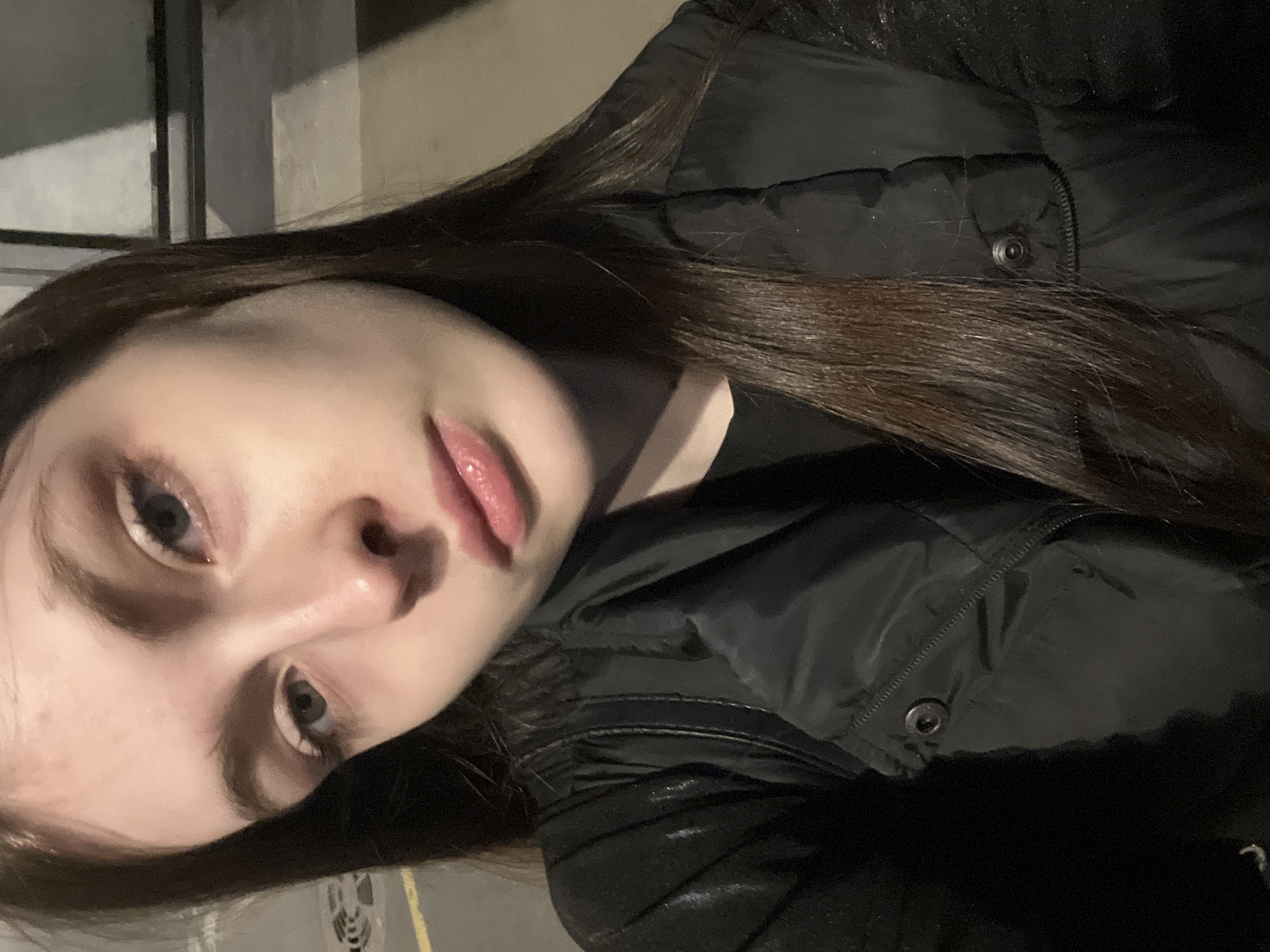 A young woman is positioned in the lower left quadrant of the image. She appears to be wearing a black puffer jacket. The background features a wall-like structure, possibly part of a building. The location cannot be determined as Saint Petersburg from the provided visual information.