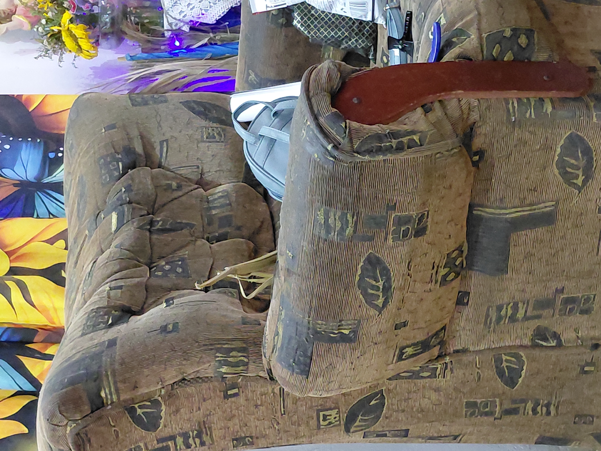 The image depicts a close-up view of a patterned brown armchair with a wooden armrest. A light blue handbag rests on the armrest. A bouquet of flowers is partially visible in the upper left corner. A table with a butterfly-themed covering sits beside the chair. The location is presumed to be Santa Ana, Venezuela. No people are visible.