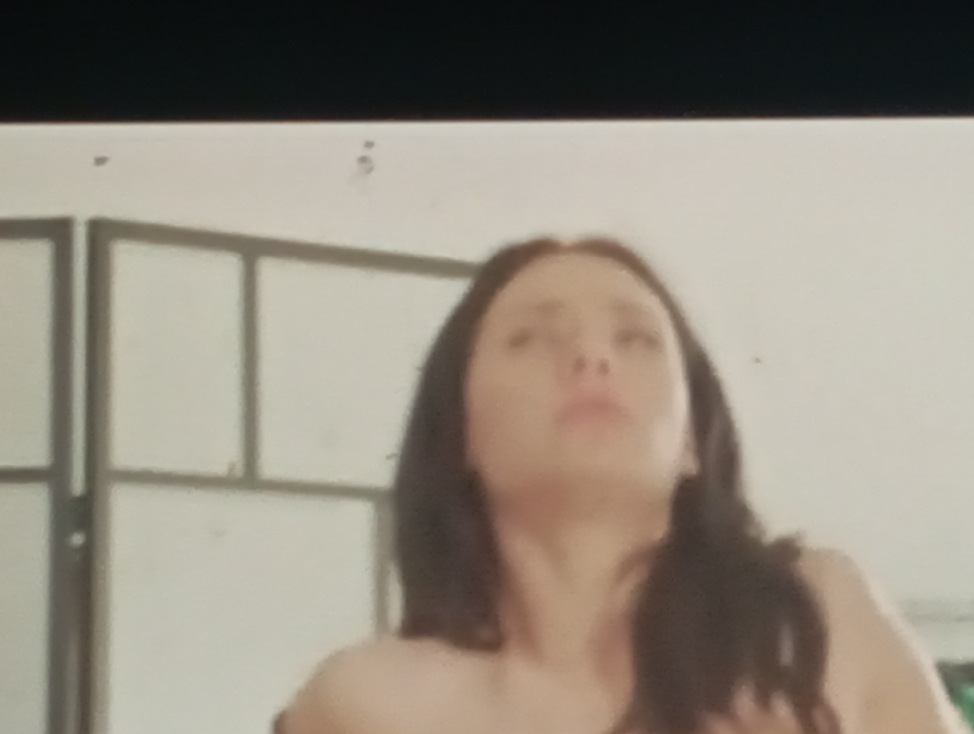 The image shows a blurred close-up of a woman's face and upper body. She has dark hair and fair skin. The background appears to be a wall with some sort of partition or screen, suggesting an indoor setting. There is no discernible information about the location in Sofiivska Borshchahivka, Ukraine, or any specific actions or interactions taking place.