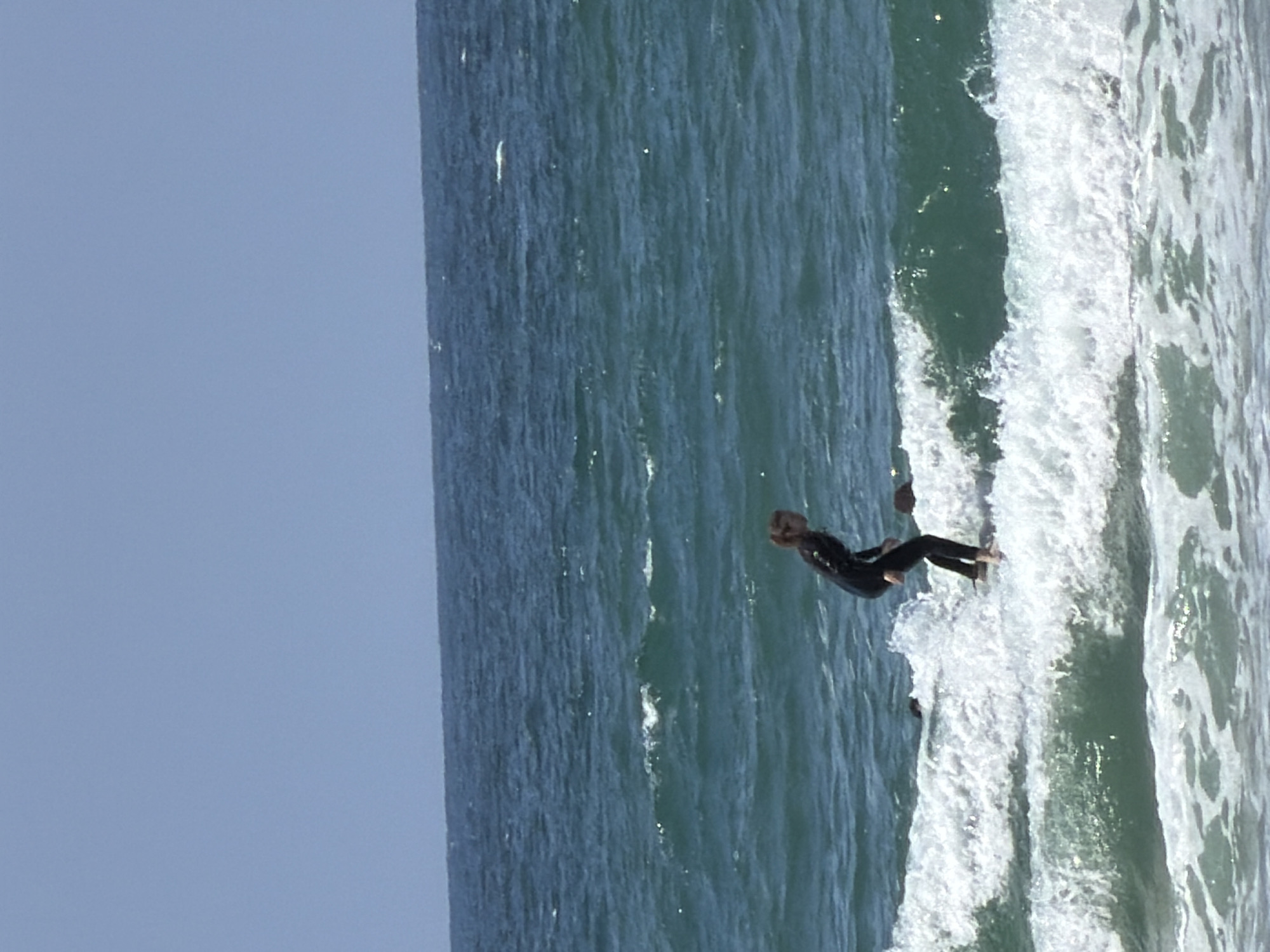 A person is seen surfing in the ocean. The sky is clear, and the ocean has white waves. The location is assumed to be Tel-Aviv, Israel.