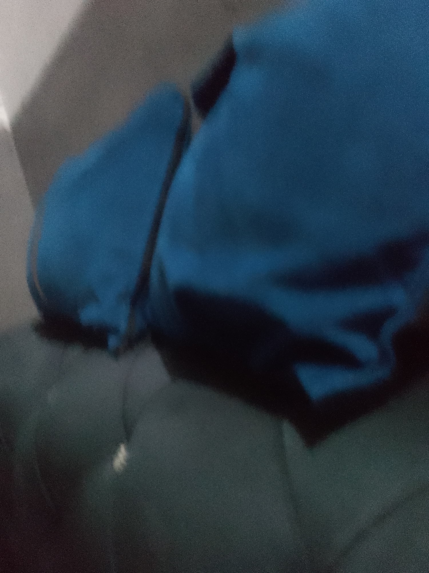 The image shows a close-up view of two large, blue fabric objects that appear to be folded or bunched up. The lighting is dim and the image has a grainy texture. The objects are placed on a dark, textured surface that could be upholstery or fabric. There is a suggestion of a lighter, possibly white, object or reflection on the dark surface in the lower center of the image. The overall impression is abstract, with the focus on the texture and form of the blue fabric. There are no discernible features of Jauro Yinu, Nigeria, in this image.