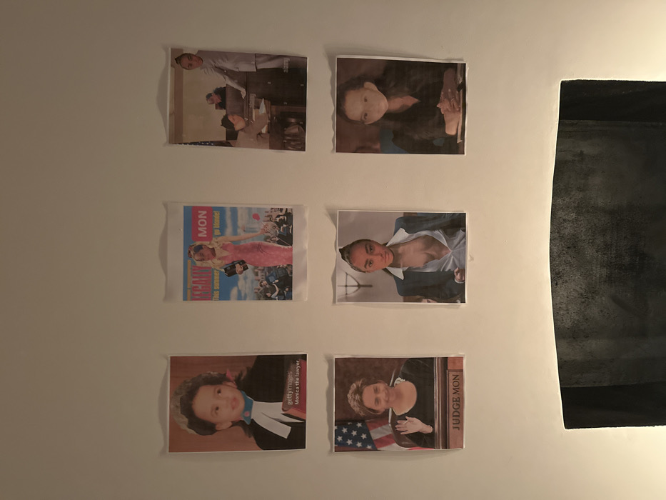 Six digitally manipulated prints are affixed to a white wall in two rows of three, illuminated from below. The images consistently feature the face of one individual, superimposed onto various subjects and scenes related to law and popular culture.
The top-left print displays a young child's face on a figure dressed as a barrister, labeled "Monica the lawyer" with a Getty Images watermark. The top-middle print shows the same child's face on a blonde woman in a pink dress holding a briefcase, with "LEGALLY MON" and "This summer go blonde!" text, reminiscent of a movie poster. The top-right print features a slightly older child's face on a person in a grey suit standing in what appears to be a courtroom, with an Alamy watermark visible.
The bottom-left print shows an adult woman's face on a judge in a courtroom setting, raising a hand, with an American flag in the background and a nameplate reading "JUDGE MON." The bottom-middle print presents the adult woman's face on a person wearing an open dark suit jacket over a white shirt, revealing cleavage. The bottom-right print depicts the adult woman's face on a person with dark hair, hands clasped on a surface.
Below the prints, a dark, textured object, possibly a fireplace mantel or a piece of furniture, is partially visible. The specific location within the city of London, United Kingdom, is not discernible from the image content.