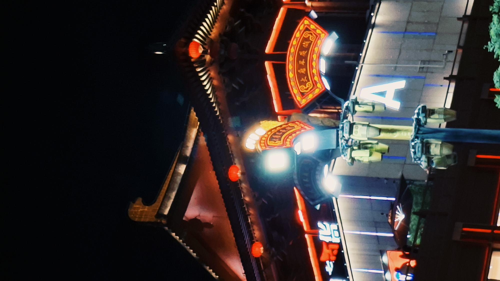 At night in Yanta District, China, a brightly lit building featuring traditional Chinese architectural elements, such as curved roofs adorned with lanterns and ornate details, intersects with modern elements including a large, illuminated "A" and a sleek, illuminated facade. The lighting scheme combines red and yellow accents with stark white illumination. The background is dark, emphasizing the contrast between the building and the night sky.