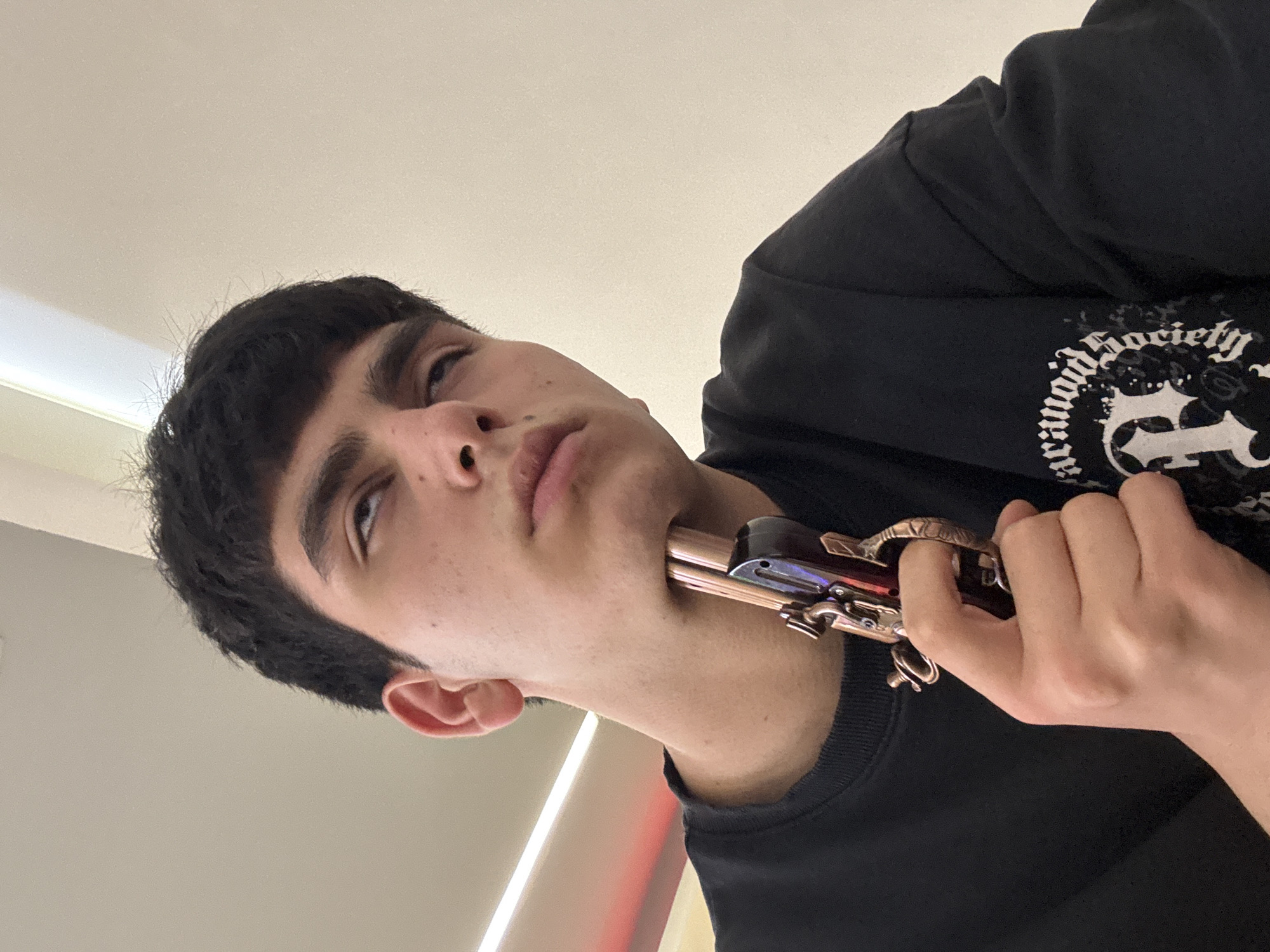 A young man is holding a pistol to his mouth. He is wearing a black t-shirt. The environment is indoors with light-colored walls. There is no definitive indication of Yerevan, Armenia.
