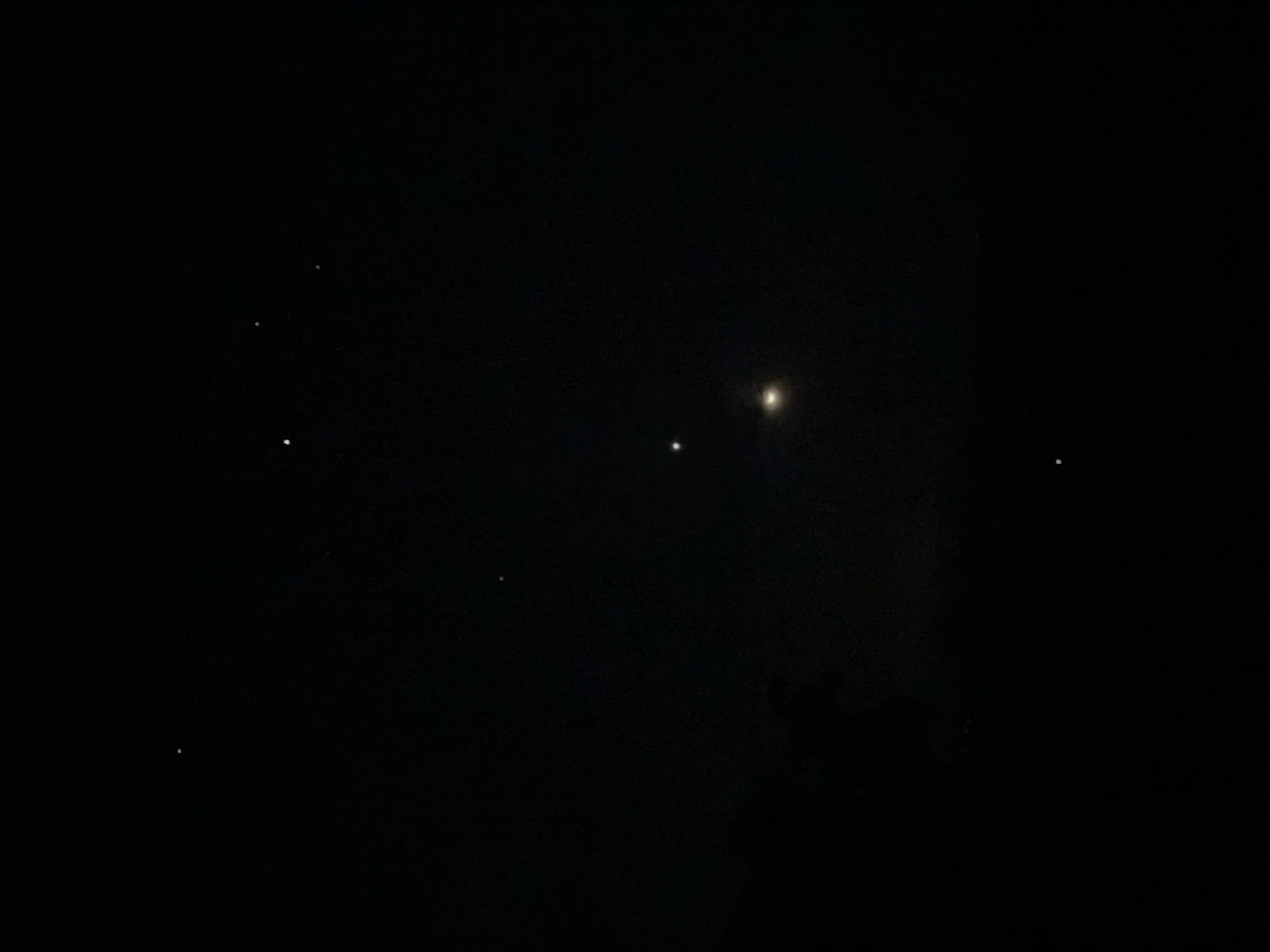 The image depicts a night sky over Nguzu Edda, Nigeria. Several stars are visible against the dark backdrop. A brighter celestial body stands out, possibly a planet or the moon. There is some indistinct dark structure in the lower half of the frame, potentially trees or terrain.