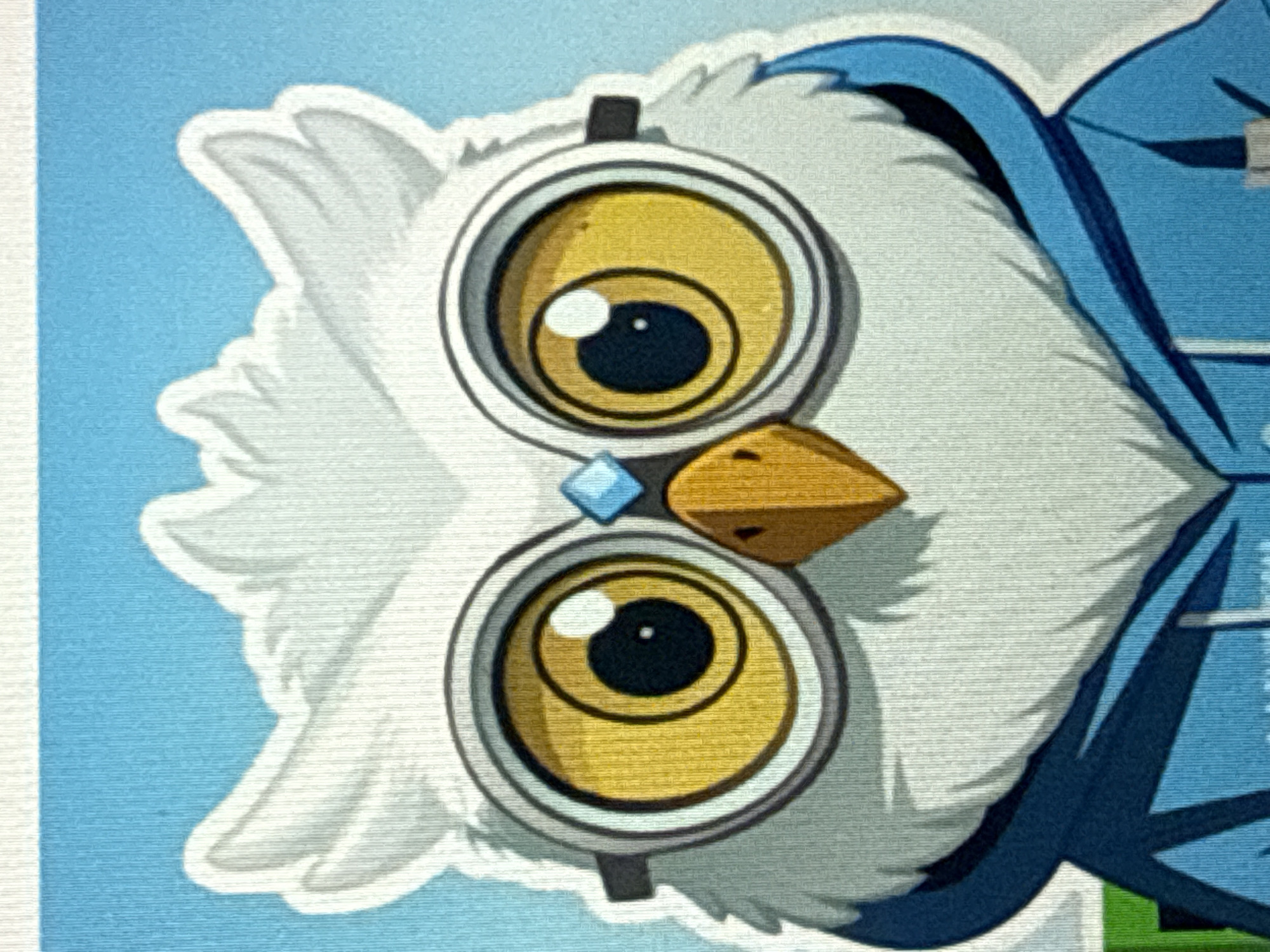 This media file is a close-up, stylized illustration of an owl's face against a blue background. The owl is depicted with large, round yellow eyes featuring black pupils and white highlights, giving it a curious or surprised expression. It wears a pair of goggles or glasses with thick gray rims, and a small blue diamond-shaped jewel is positioned between its eyes. The owl's beak is a sharp, golden-brown triangle. The owl has white, fluffy feathers around its face and head, and is wearing a blue garment with dark blue trim, suggesting it might be dressed in clothing or a costume. The illustration style is cartoonish with bold outlines and flat colors, but with a textured appearance, possibly mimicking a painting or print. The background is a solid, light blue, with a hint of a lighter blue gradient on the left side. There are no visible text elements. The image does not provide specific details about the time of day, weather, or explicit location cues beyond the provided context of Sochi, Russia, which would likely be inferred from the artwork's origin or presentation rather than visual elements within the image itself. The focus is solely on the character's face and immediate surroundings.
