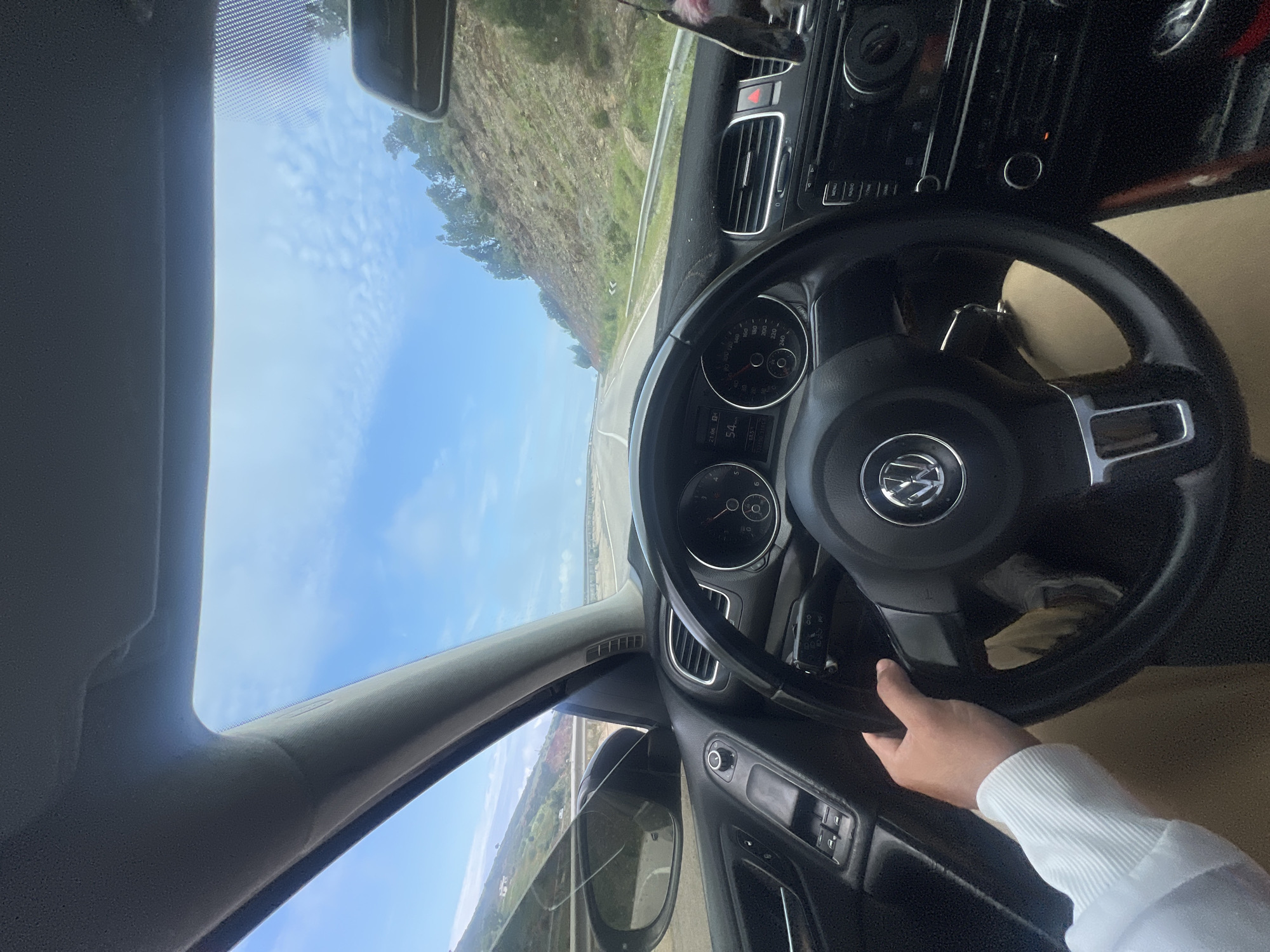 The view is from inside a car, looking forward through the windshield. The car is moving on a road near Zaouiat Sidi Kacem, Morocco. A driver's hand is visible on the steering wheel. The landscape outside includes a road, sky, and foliage. The car's dashboard, steering wheel, and side mirrors are prominent features in the frame.