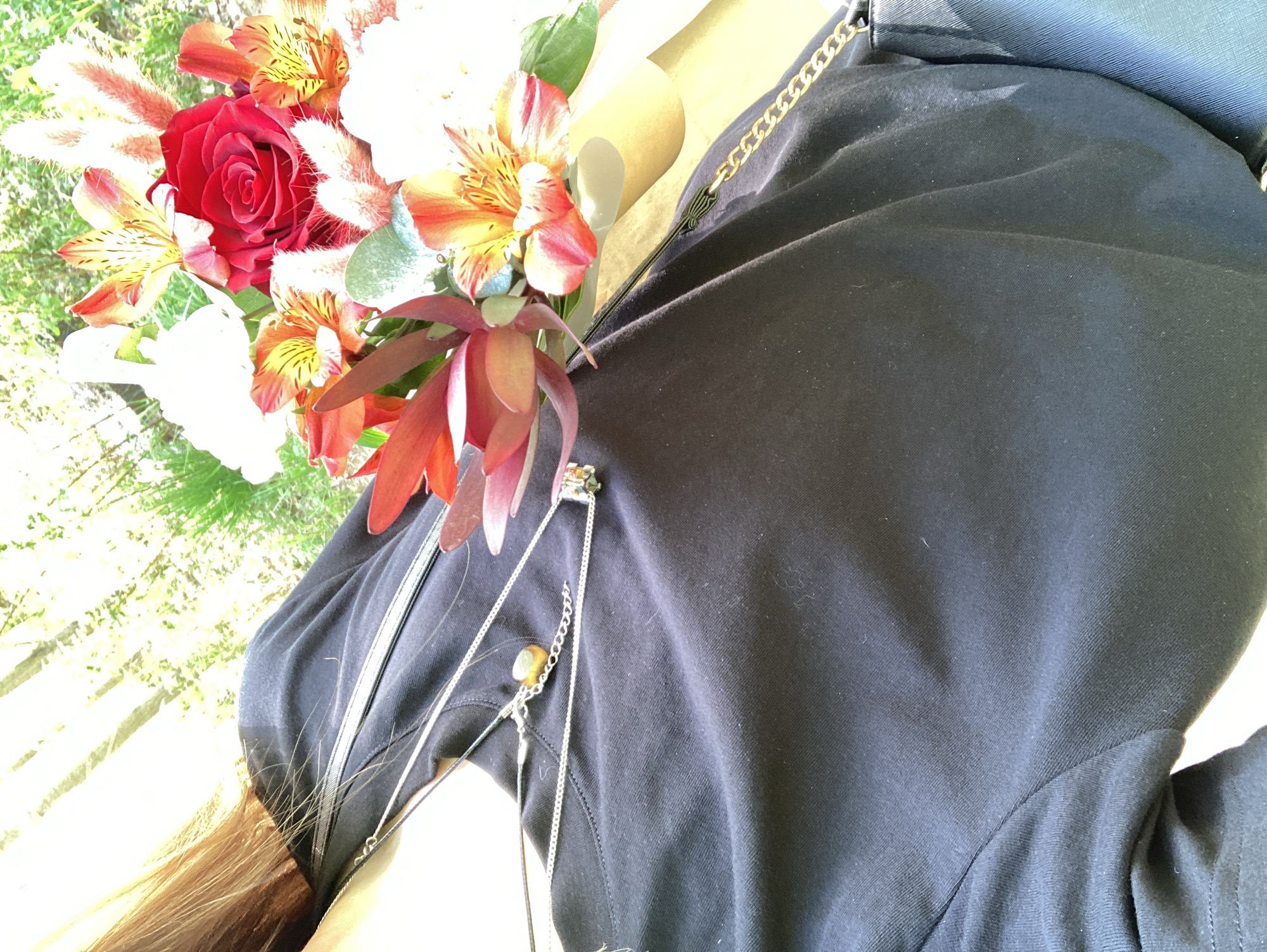 The image shows a person holding a bouquet of flowers with red, orange, and white blooms. The person is wearing a dark-colored shirt with a silver-colored chain and pendant. The location of Chaikovsky, Russia cannot be determined from the content of this image.
