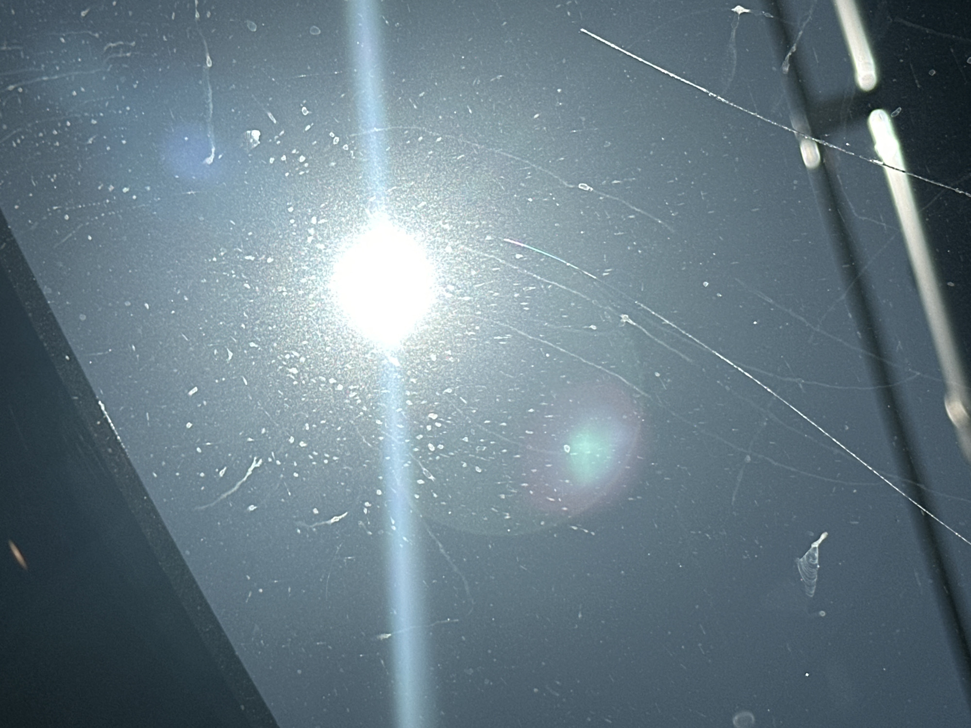 The image shows a close-up of a scratched and dusty dark surface, likely glass or plastic. Bright light reflects off the surface, obscuring details. There are no people, actions, or location indicators visible. The context of Moscow, Russia is not determinable from the image.