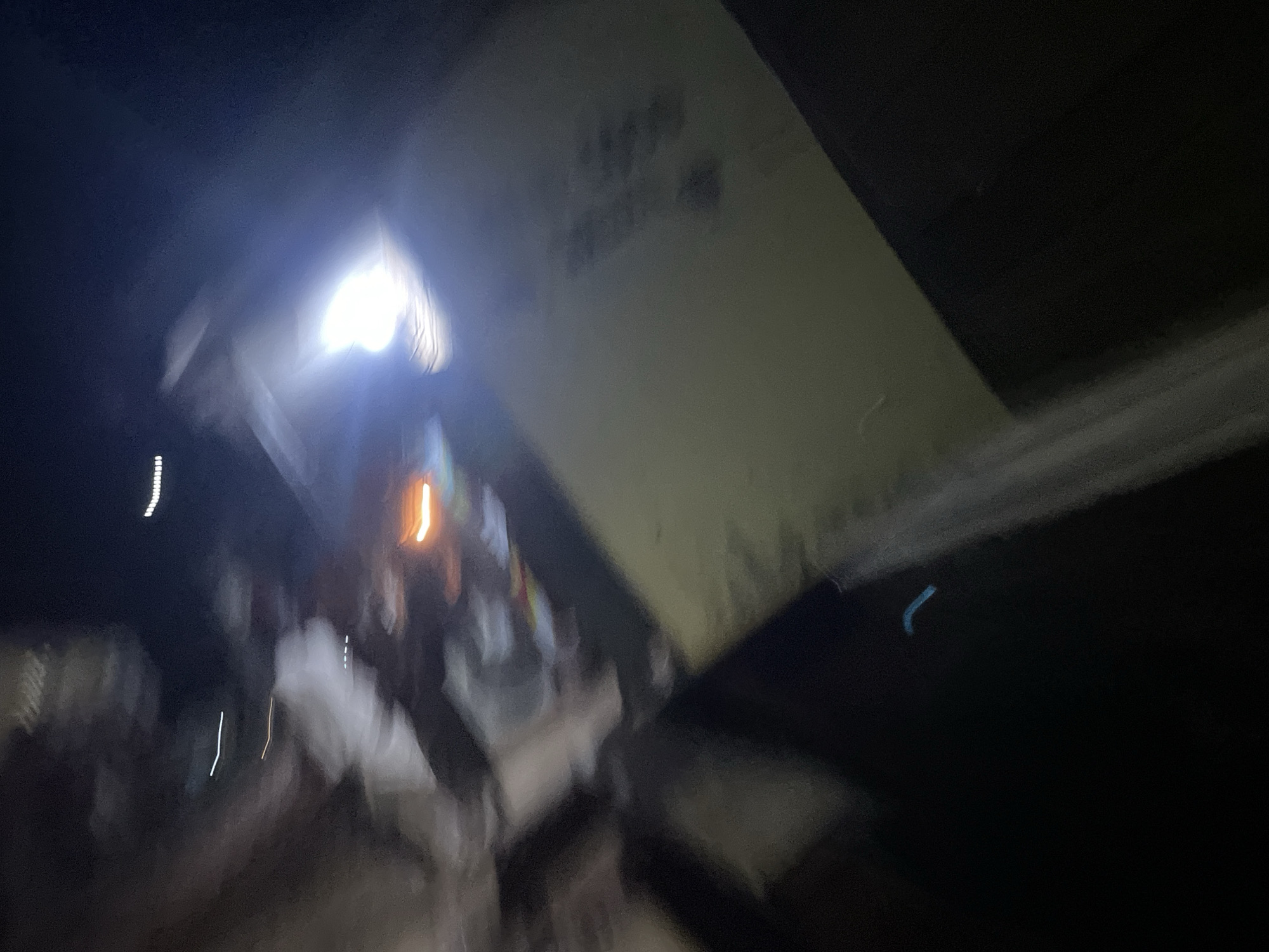 The image depicts a blurred scene, likely taken at night, possibly in a vehicle given the motion blur. There are several bright light sources, including what appears to be a strong headlamp or spotlight illuminating a light-colored surface. In the background, there are streaks of light, suggesting movement. The overall impression is of a dynamic and potentially disorienting environment. Without more context, it's impossible to pinpoint the exact location in Lokoja, Nigeria, but the presence of a bright light and potential movement suggests an outdoor setting or a well-lit interior with external light sources.