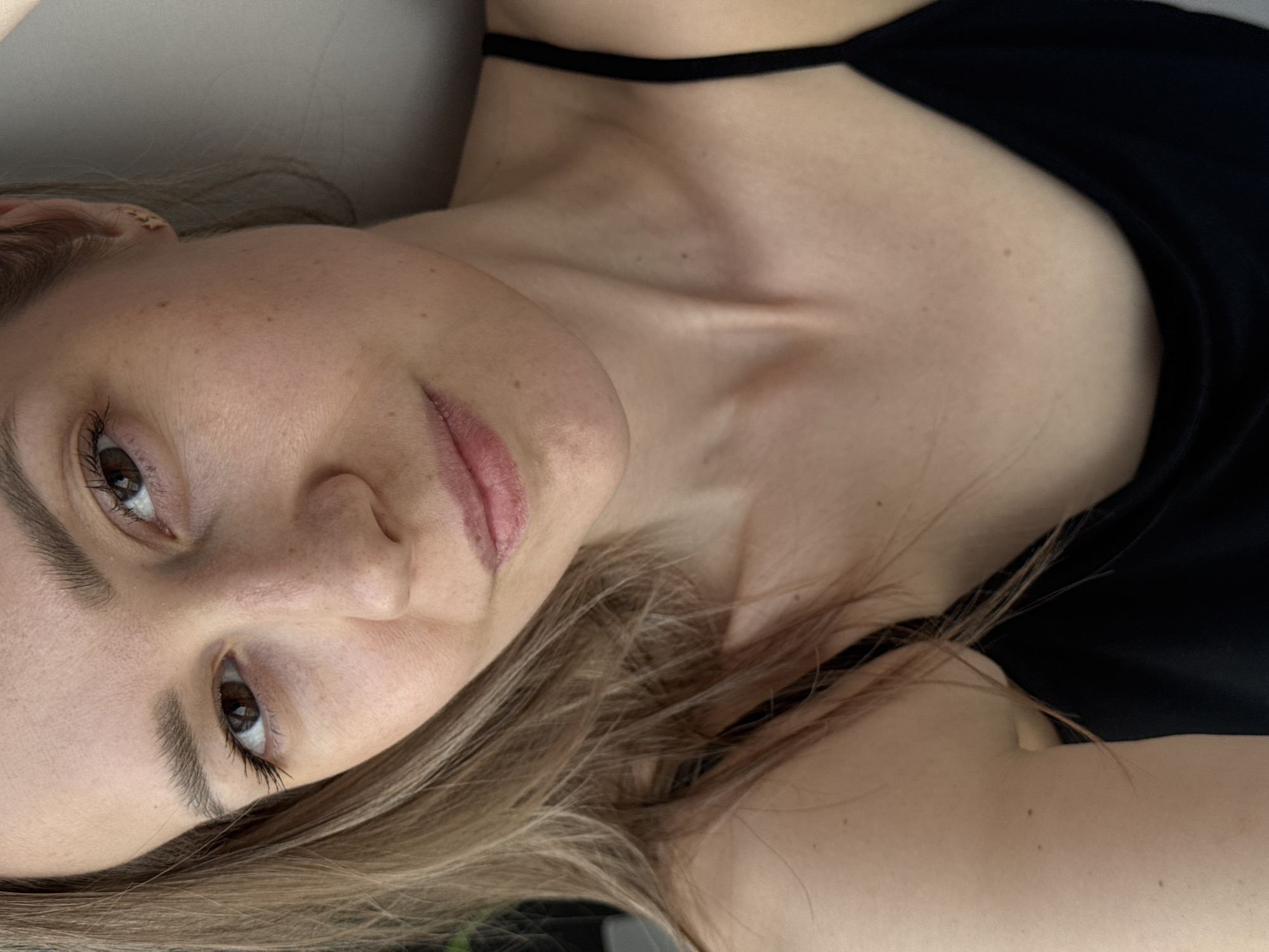 A close-up shot depicts a fair-skinned woman with light brown hair, lying down. She has brown eyes, freckles on her face, and is wearing a black top with thin straps. The focus is on her face and upper body. There is no discernible information about the location being the city of Chaikovsky, Russia.