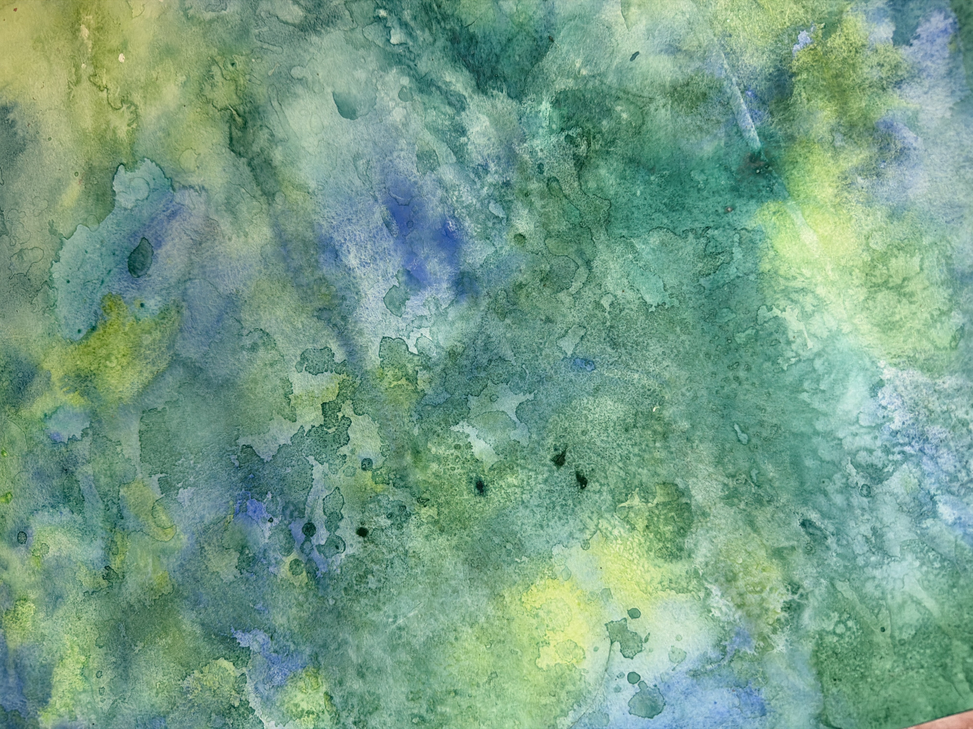 This is a close-up abstract watercolor painting. The painting is dominated by shades of green and blue, with some yellow hues interspersed. There are areas of intense color and lighter washes, creating a sense of depth and texture. The paint has been applied in a way that creates organic, splotchy shapes and some darker, almost black, spots. The background appears to be watercolor paper. There is no discernible location in the city of Ufa, Russia, as this is an abstract artwork.