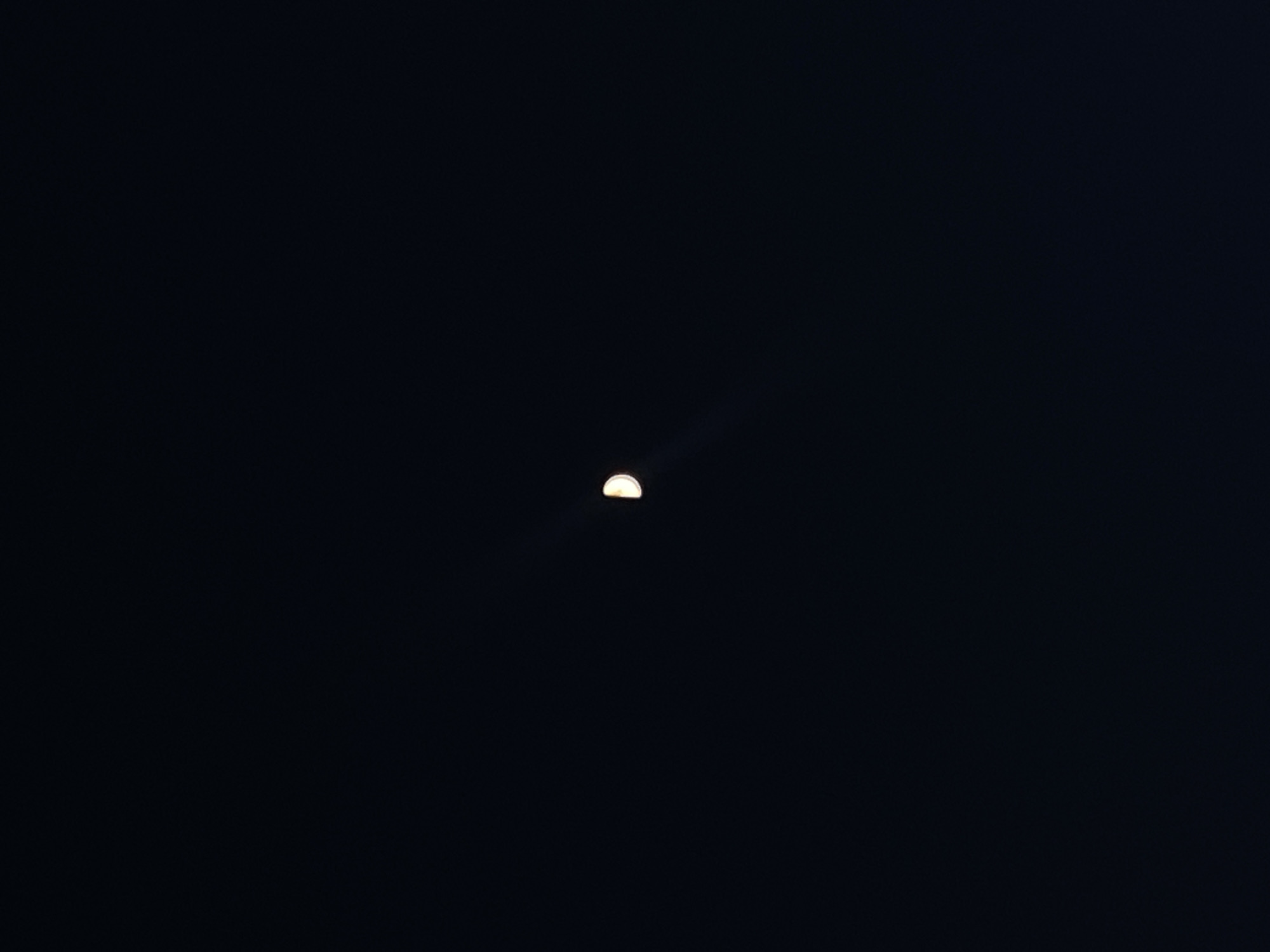 The image shows a crescent moon in the night sky. The background is dark. The photo appears to be taken in Шебунино, Russia, but the image itself doesn't provide any visual confirmation or detail to prove it to be in this location.