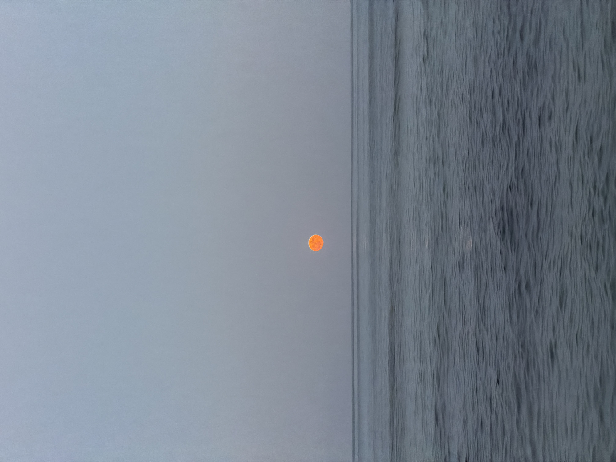 This is a vertically oriented, eye-level photograph of the ocean at dusk. The sky occupies the top half of the frame and is a pale, muted gray with a slight gradient towards a lighter shade near the horizon. Centered on the horizon, a vibrant, glowing orange circle, presumably the sun or moon, is visible. The ocean takes up the bottom half of the image and is a deep, cool blue-gray, with subtle ripples and waves creating texture. The horizon line is sharp and divides the sky and sea. The scene is devoid of any people, structures, or vessels, conveying a sense of vastness and tranquility. The location is specified as Golden Beach, Greece.