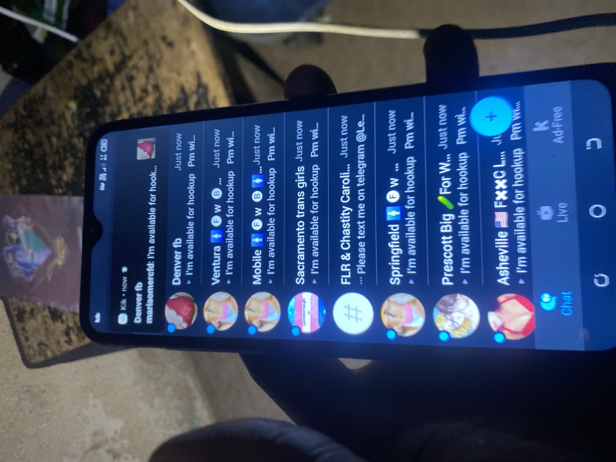 The image shows a close-up of a smartphone screen displaying a Kik messaging app interface. The chat list features various profiles with names like "Denver fb," "Ventura," "Mobile," "Sacramento trans girls," "FLR & Chastity Caroli...," "Springfield," "Prescott Big," and "Asheville FXXC L." Each profile displays the message "I'm available for hookup Pm wi..." or similar variations indicating a focus on hookups. The profiles have images of women. The city of Bukuru, Nigeria, is not discernible in this image.
