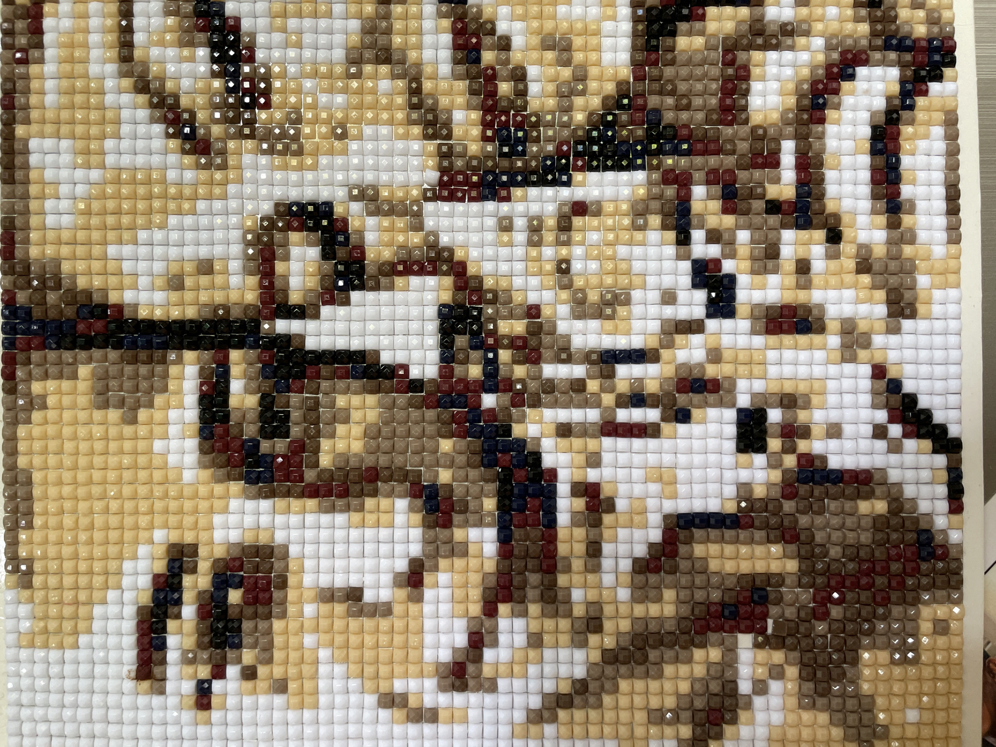 The image shows a close-up of a partially completed diamond painting. The canvas is covered with a grid of small, square, multi-faceted plastic gems. The gems are various colors, including white, tan, brown, dark blue, and red. The pattern seems to be a complex design, though the overall subject is not immediately apparent due to the close-up view. The background is white.
I don't have information about the location in the city of Kuta Selatan, Indonesia. The image only shows the diamond painting itself.