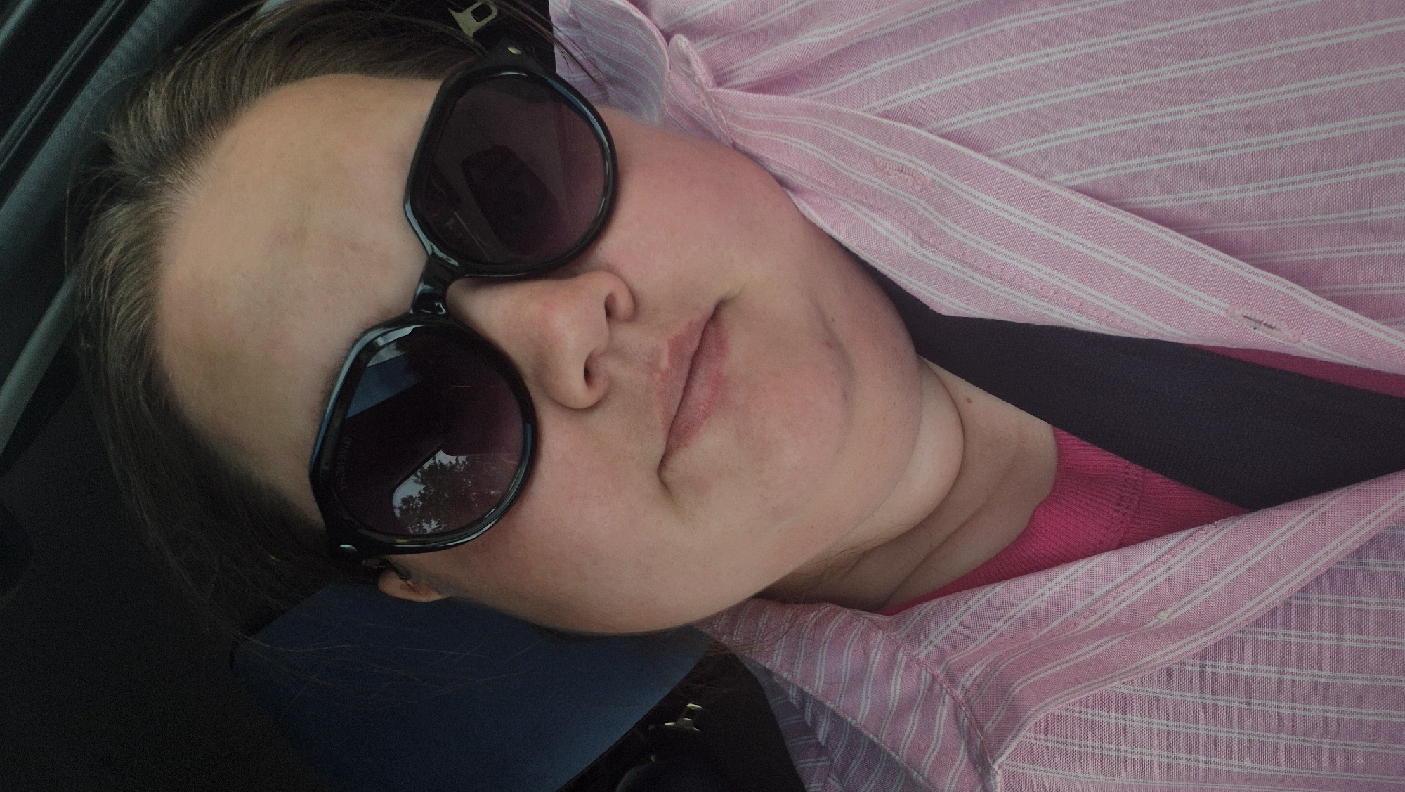 A person with light skin is shown wearing sunglasses and a pink and white striped shirt. A seatbelt is visible across the person's chest. The individual appears to be inside a vehicle. There is no contextual information provided that identifies the location of the city of Chaikovsky, Russia.