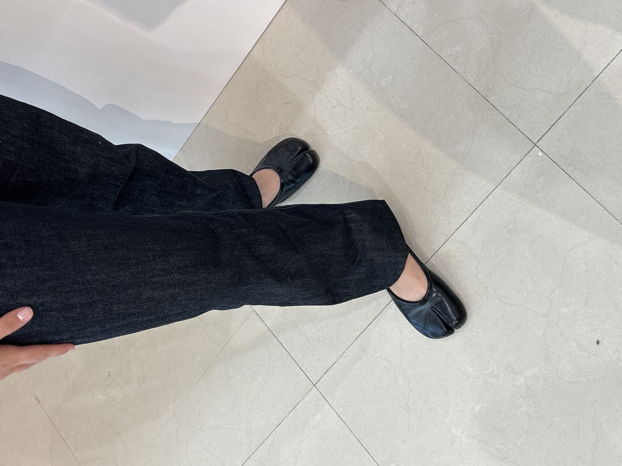 A person wearing dark jeans and black split-toe shoes stands on a light-colored tiled floor. The person's hand is visible near the bottom left corner of the image. The scene appears to be indoors. The location is not San Francisco Ocotlán (Ocotlán), Mexico.