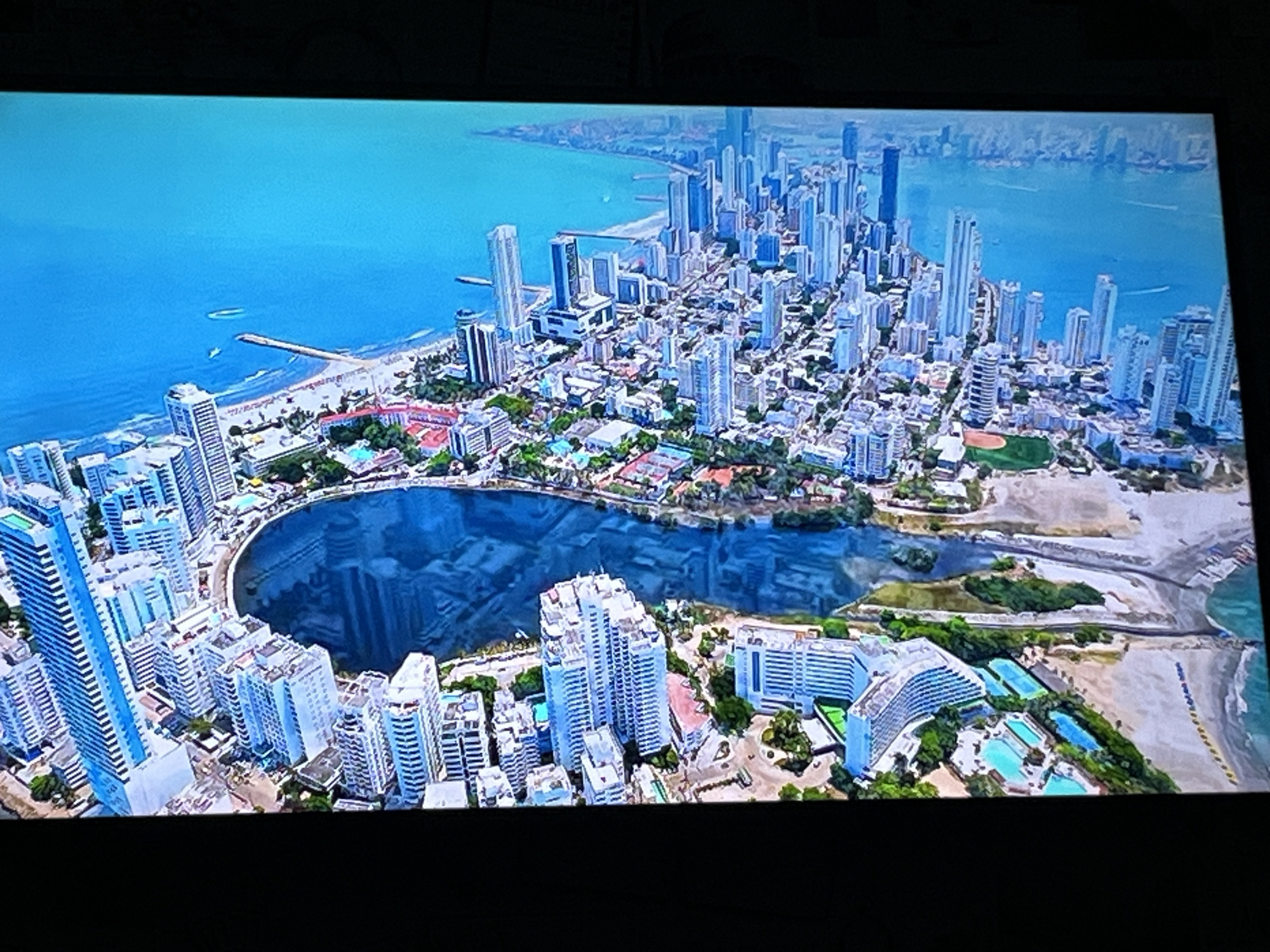 This is an aerial view of a coastal city with numerous high-rise buildings and a large body of water. The buildings are predominantly modern, with many appearing to be residential or hotel complexes, characterized by their white or light-colored facades and varying heights. Some buildings have balconies, and a few are shaped in curved or stepped designs.
The city is situated along a coastline with a beach and the ocean. The water is a vibrant blue, and there are signs of human activity such as small boats on the water and beach umbrellas or loungers on the shore. A prominent feature in the foreground is a large, irregularly shaped lagoon or bay, connected to the ocean. The water within this lagoon is a deep blue and reflects the sky and surrounding buildings.
Greenery, in the form of trees and landscaped areas, is visible interspersed among the buildings and along the coastline, particularly around the lagoon and in resort-like areas with swimming pools. Some of these areas appear to be recreational, with swimming pools and possibly tennis courts.
The overall impression is of a well-developed, modern city that combines urban living with coastal tourism and recreation. There are no people clearly visible in this aerial shot, and the focus is on the urban landscape and its integration with the natural environment.
This image is not of Kharkiv, Ukraine. Kharkiv is an inland city and does not have a coastline or this type of coastal architecture.